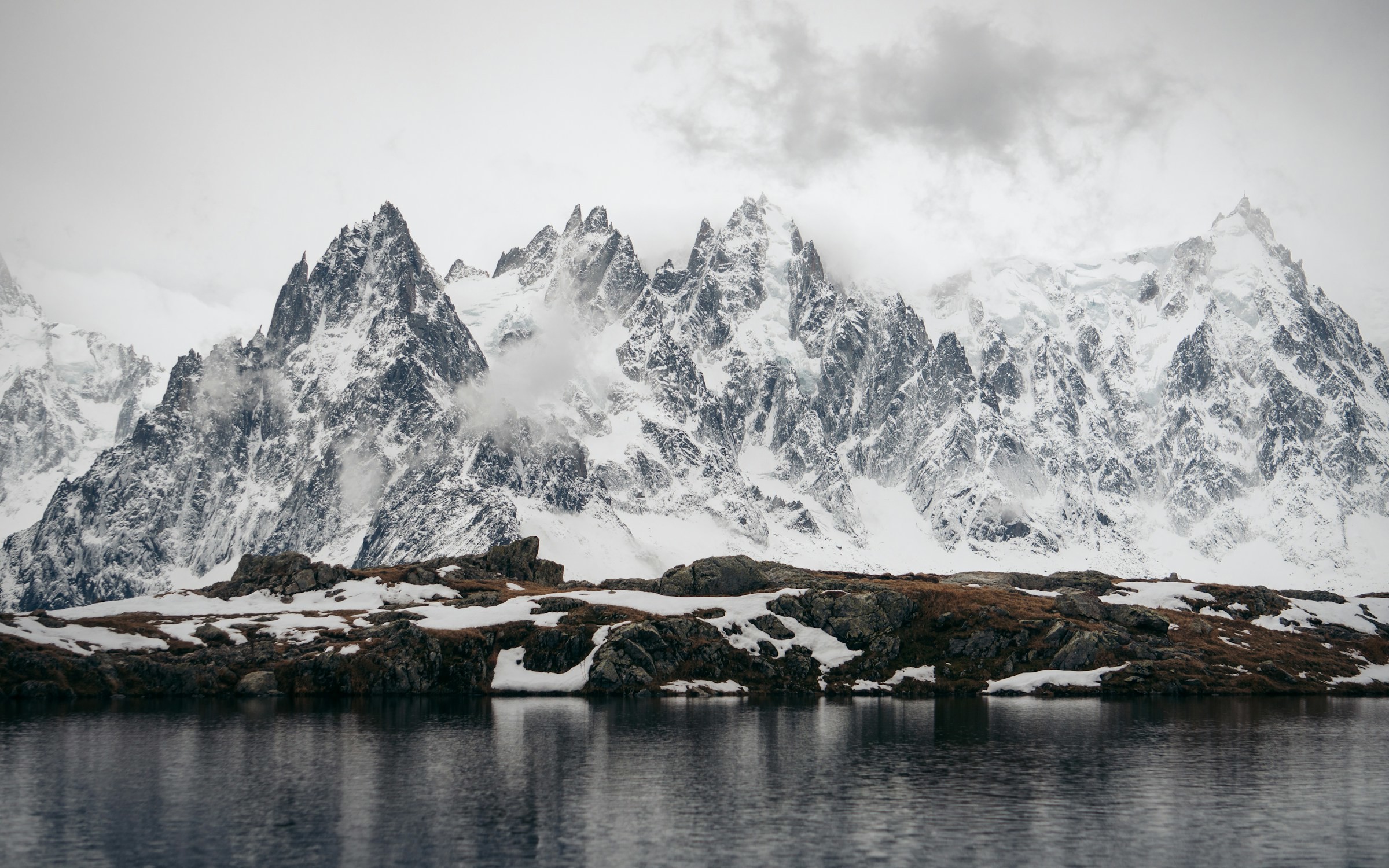 Sjö vid foten av ett mäktigt snötäckt berg mot en vit himmel i Chamonix, Frankrike