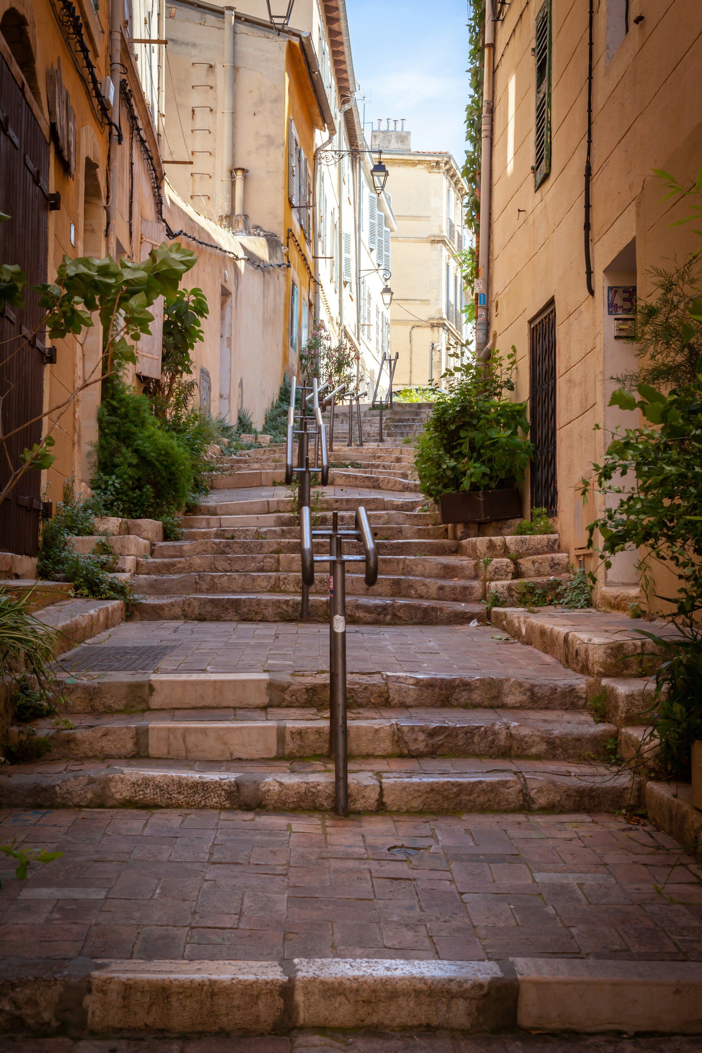 Stenbelagd trappa i europeisk gränd omgiven av traditionella byggnader med grönska i Marseille.