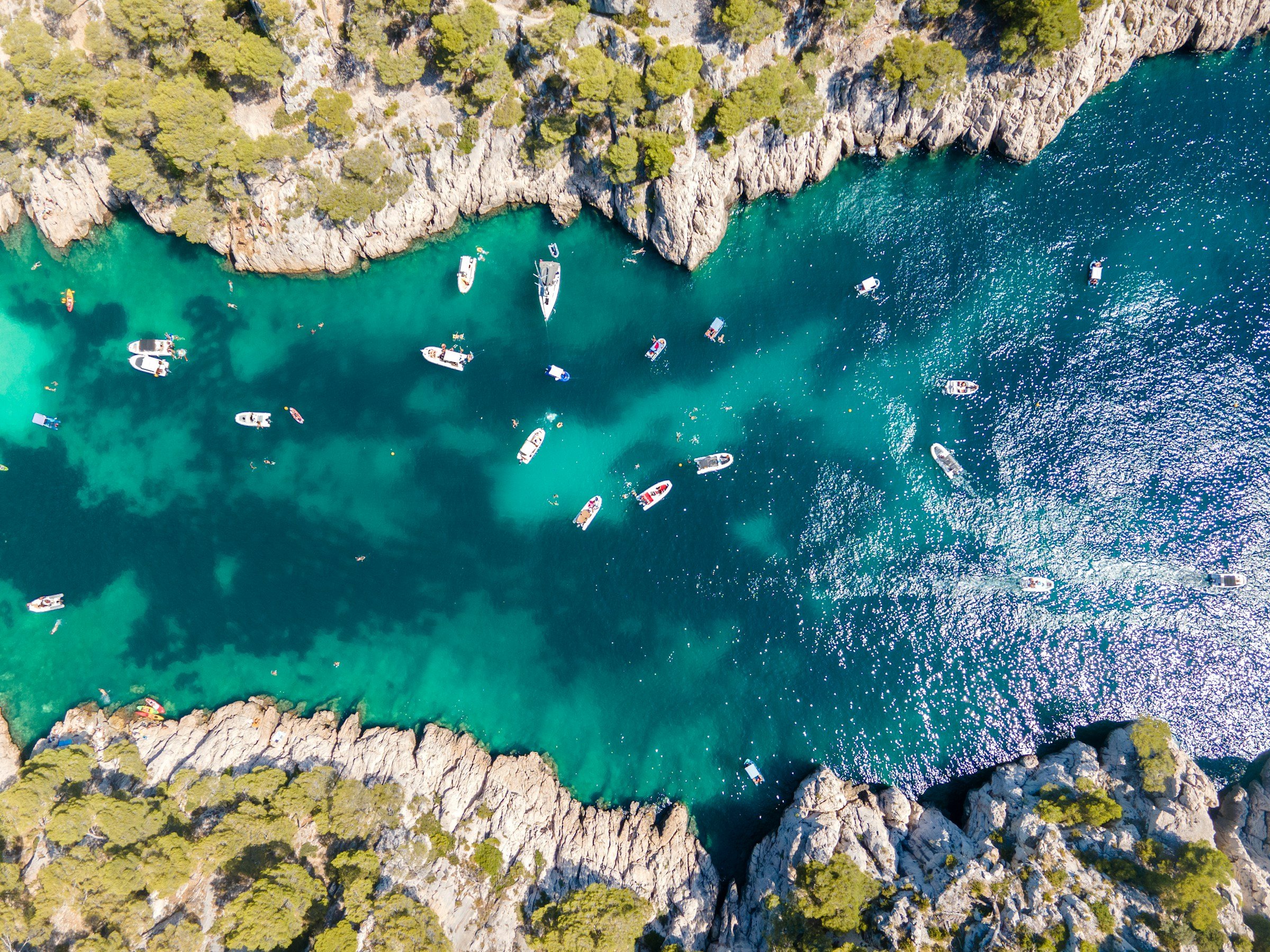 Flygbild av båtar som ankrar i det klara turkosblå vattnet vid en klippig kustlinje i Marseille.