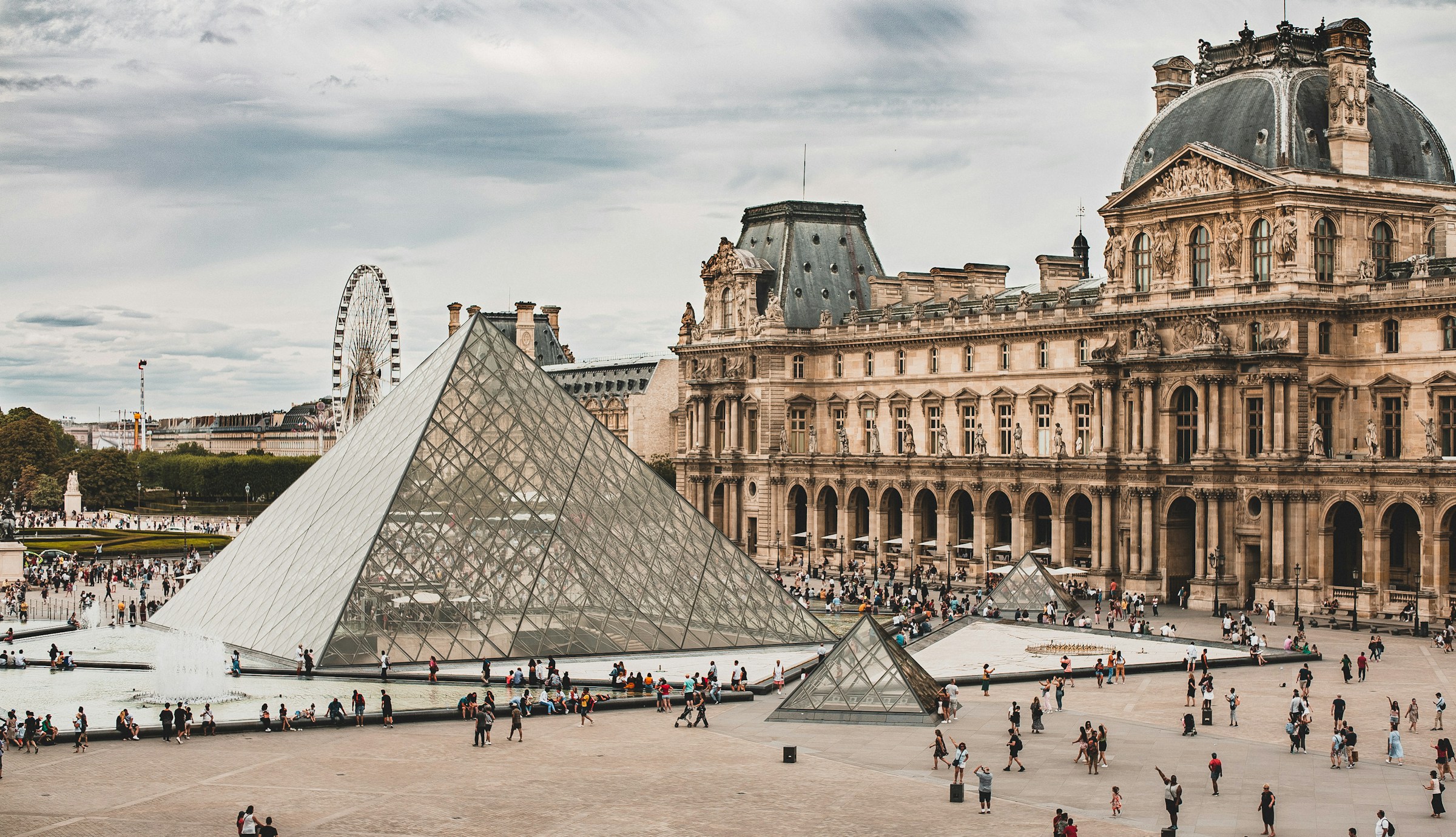 Vy över Louvren och dess glaspyramid, med människor och pariserhjulet i bakgrunden, Paris.