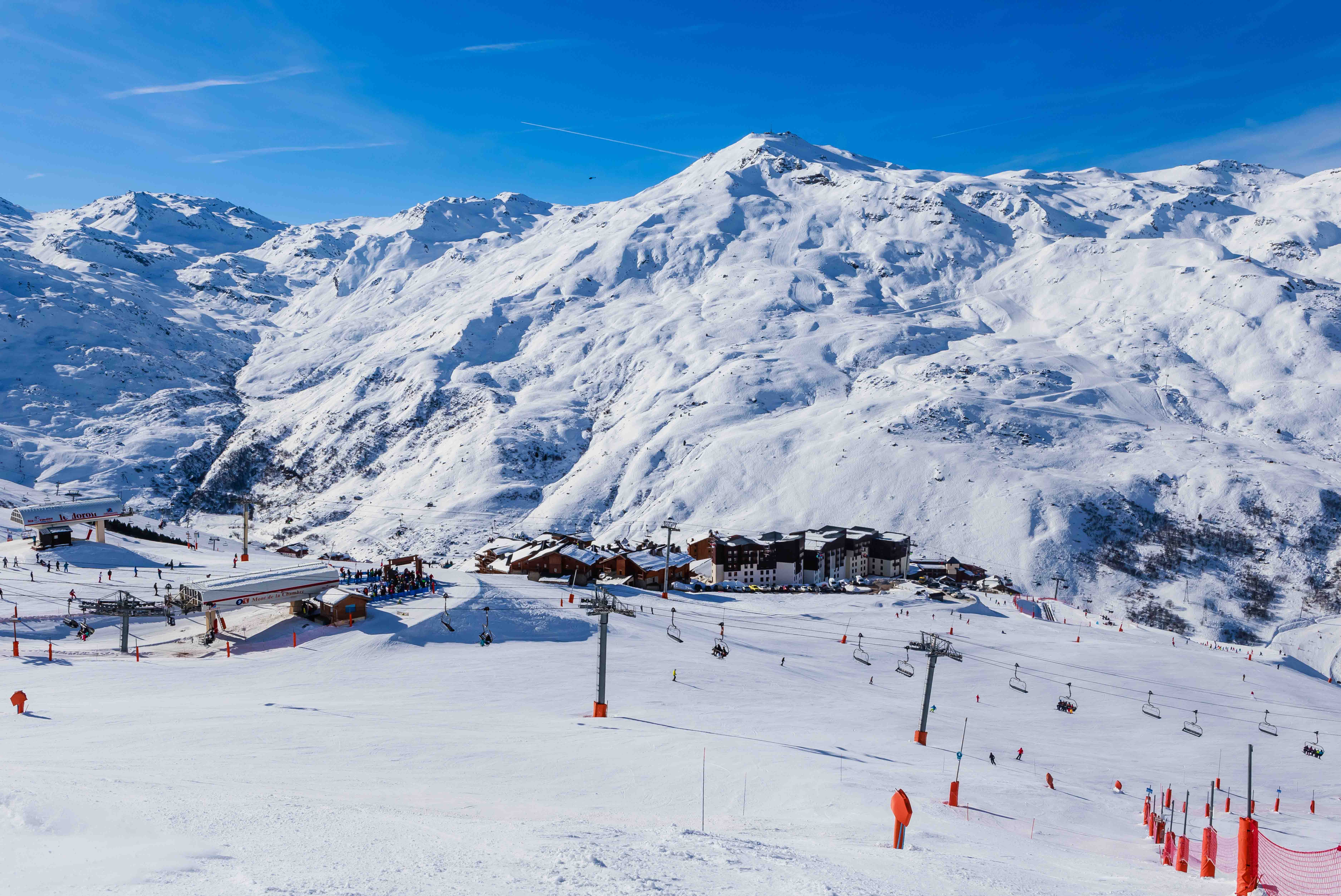 Resa till Val Thorens - Vinterlandskap med skidbackar och liftar i en snöbeklädd bergsort, skidåkare njuter av soligt väder.