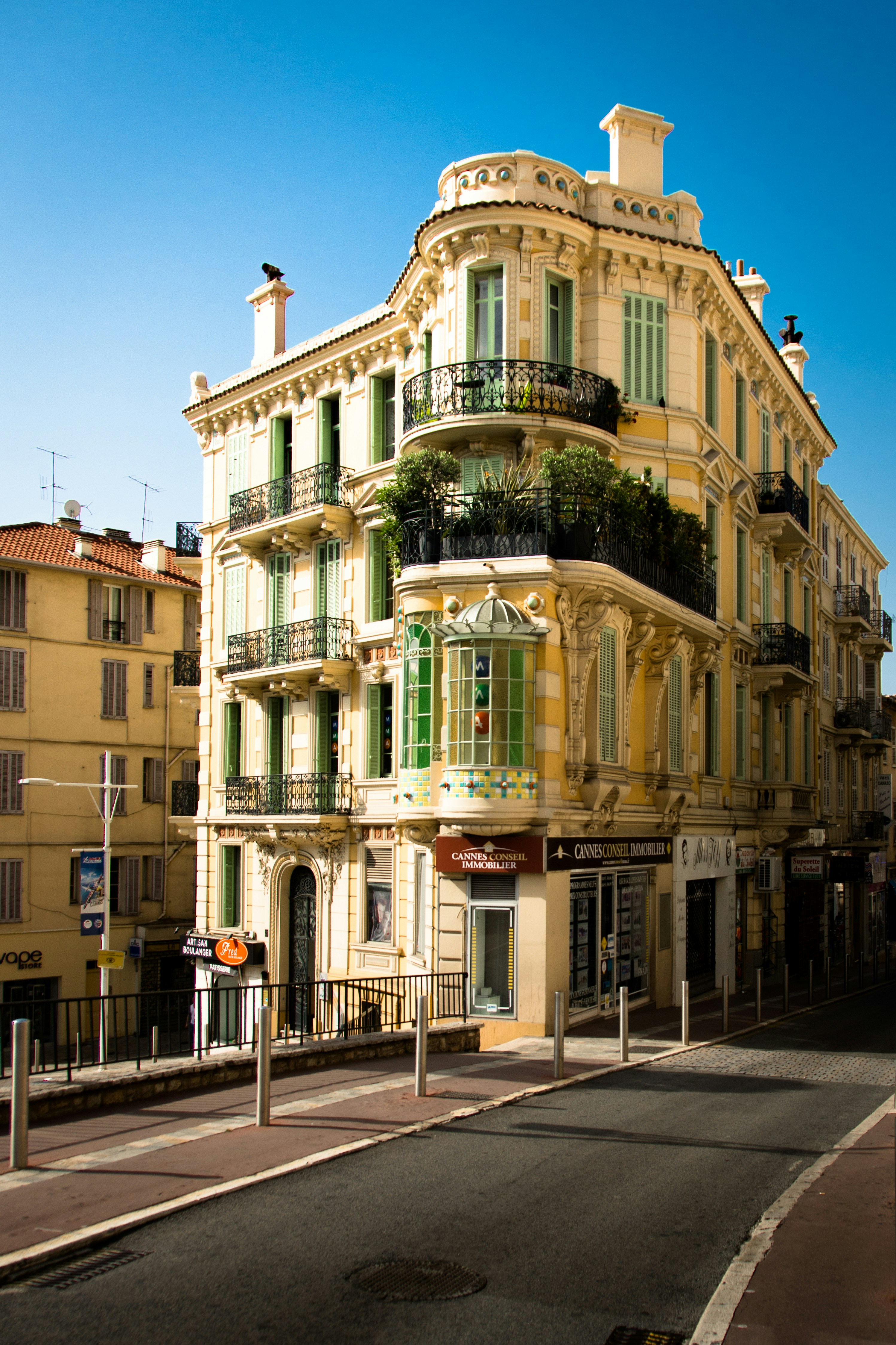 Vackert gul fasad på ett traditionellt europeiskt stadshus med balkonger och gröna växter under en klarblå himmel i Cannes.