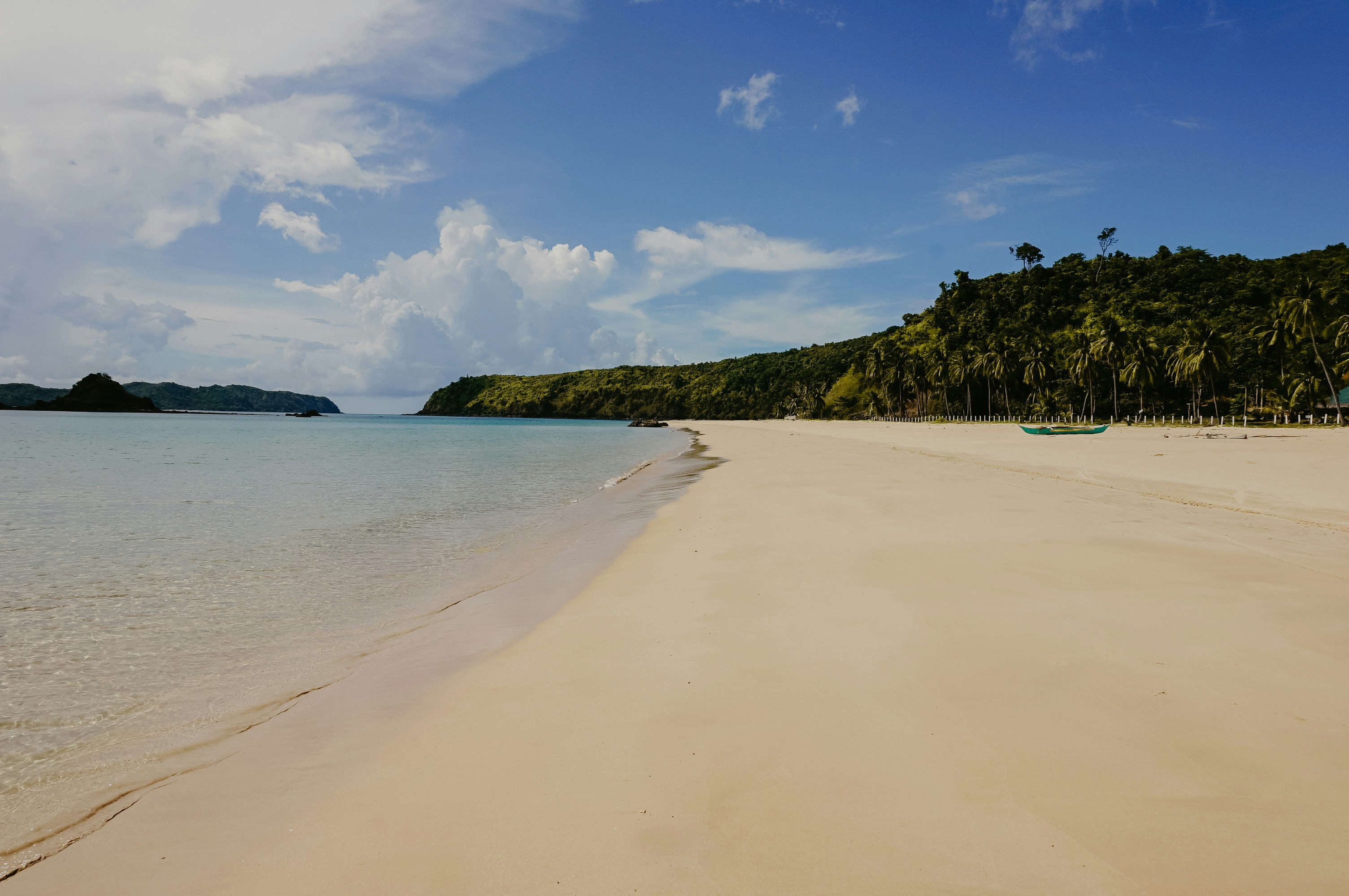 Öde tropisk strand med fin vit sand, lugnt vatten och frodig grönska på en solig dag i Guadeloupe.