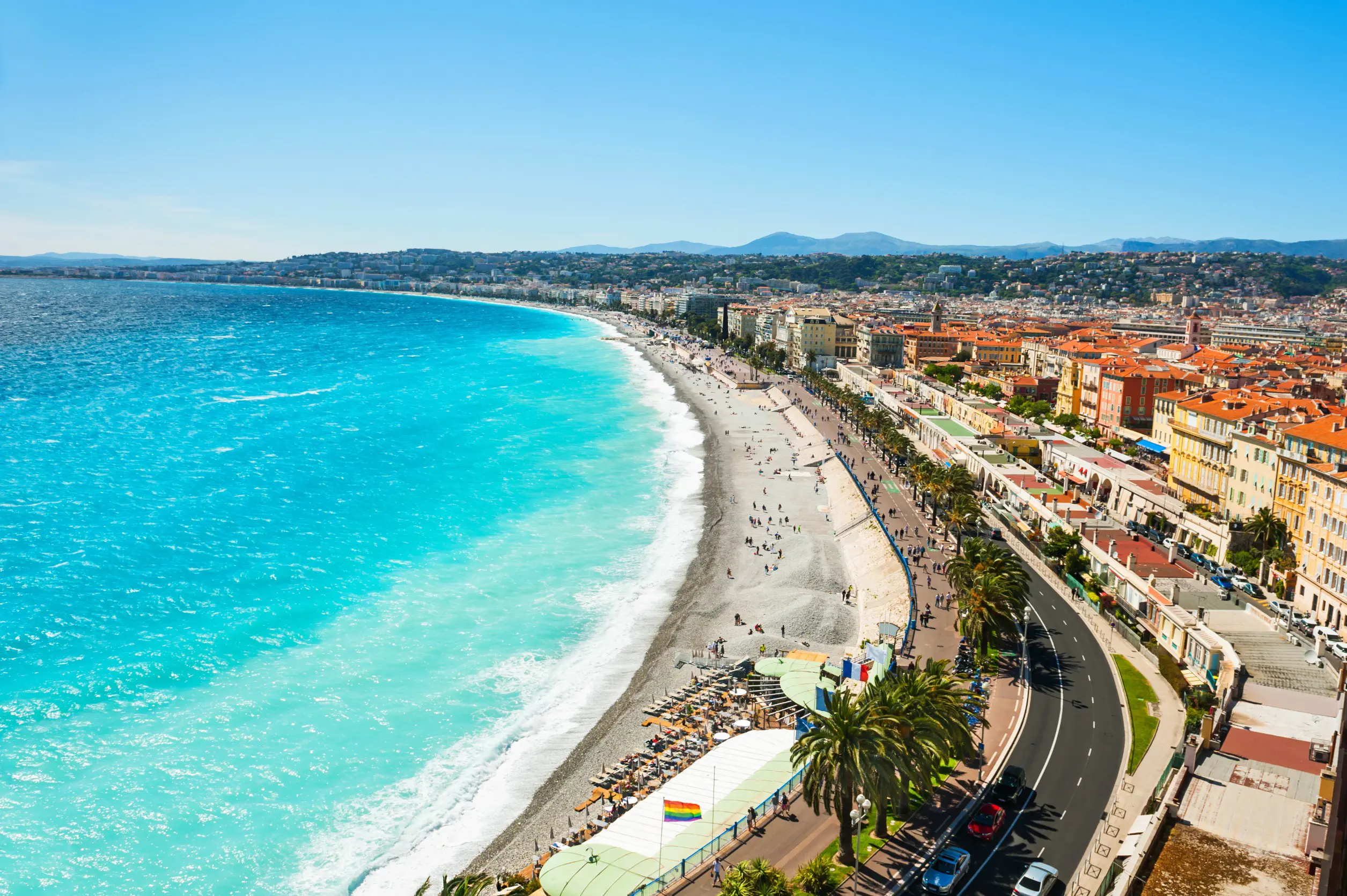 Resa till Nice - Luftvy av kurvig kustväg och strandpromenad vid en livlig strandstad med turkost hav.