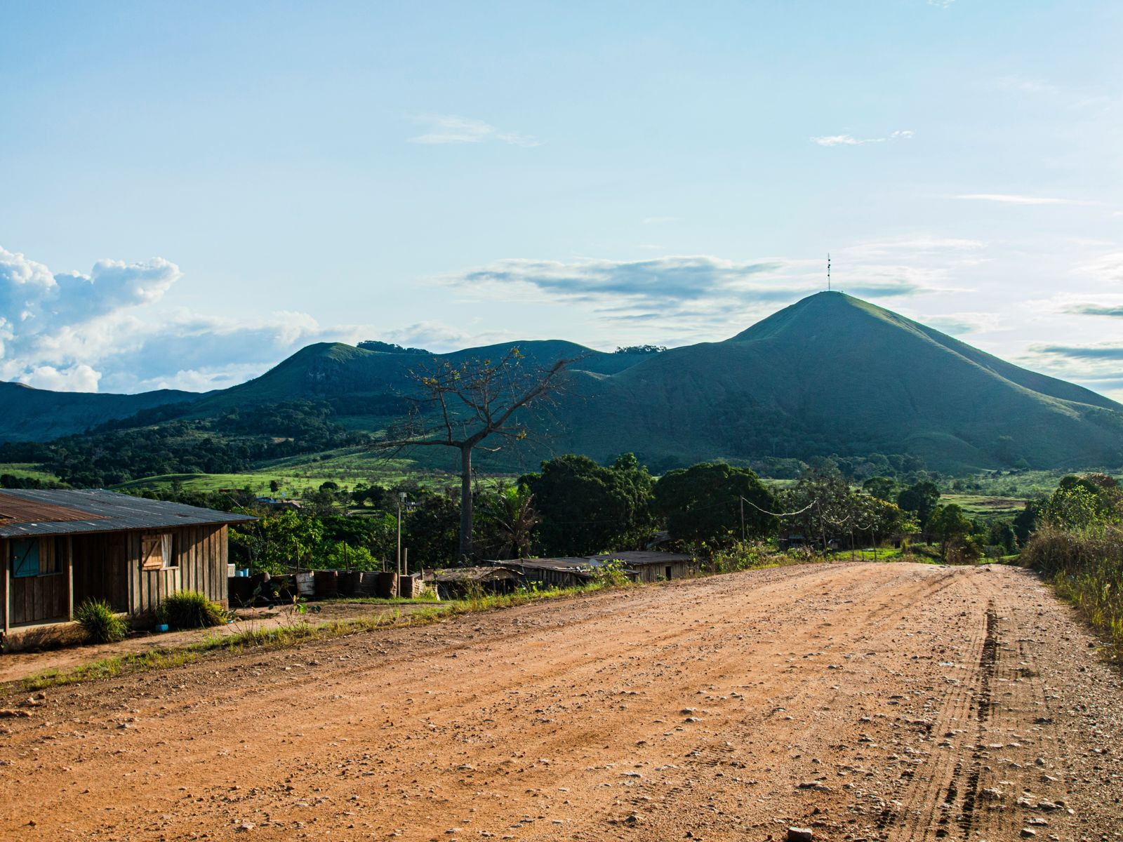 Resa till Gabon - Grusväg som leder genom landsbygd med gröna kullar och berg i bakgrunden på en klar dag.