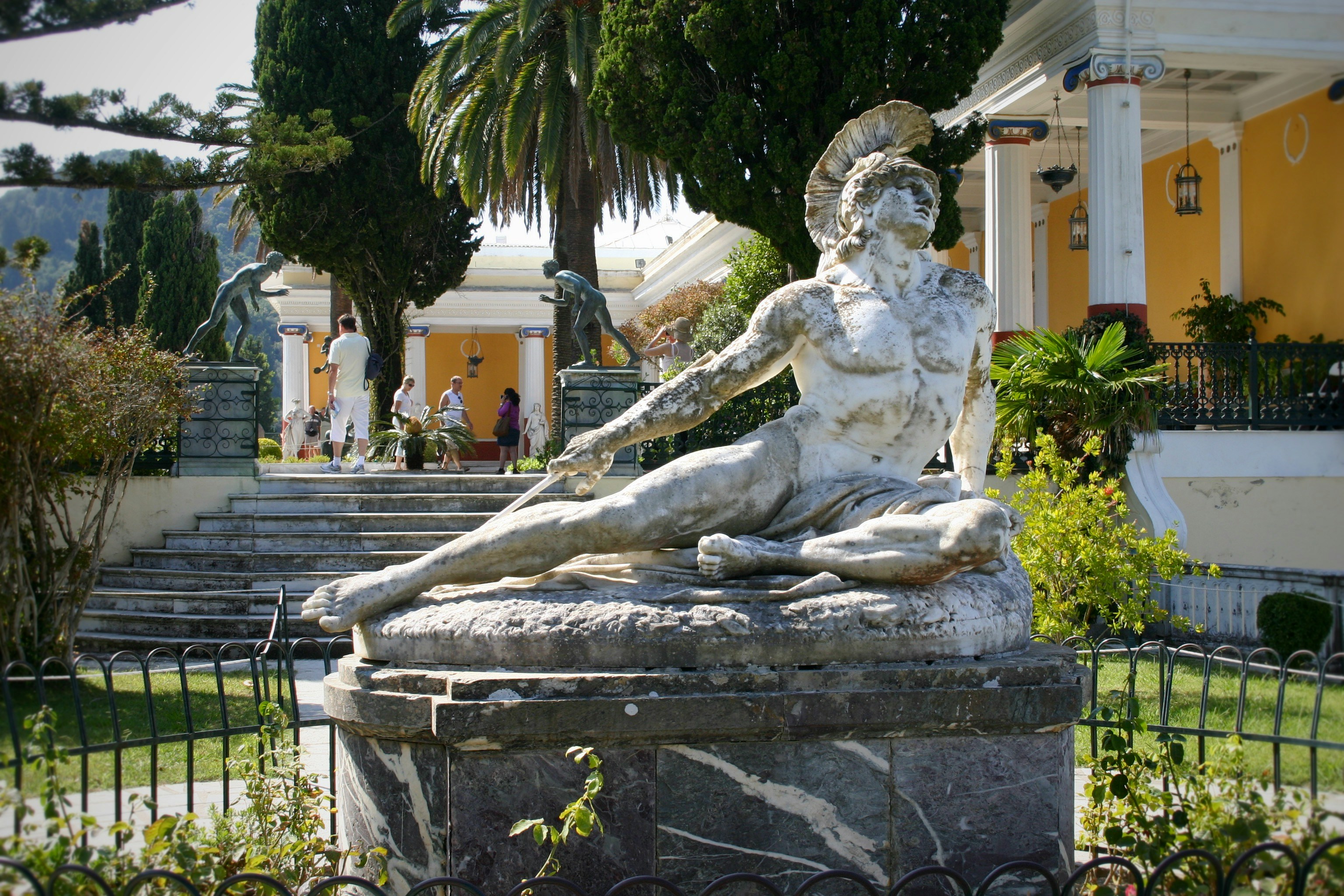 Antik marmorskulptur i klassisk trädgård framför elegant gult hus på Korfu i Grekland