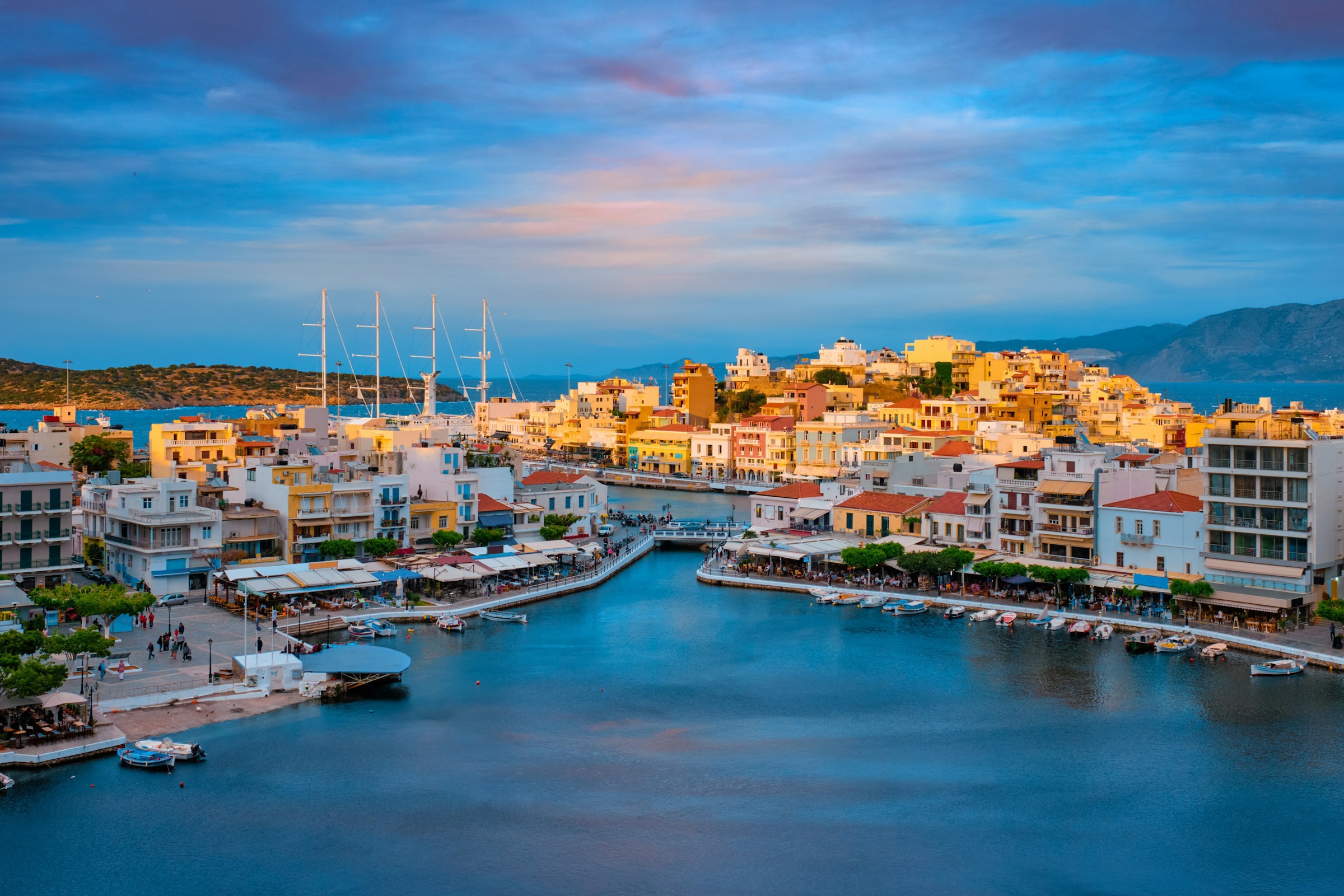 Chania på Kreta vid solnedgången med färgglada byggnader, segelbåtar och en promenad längs vattnet.