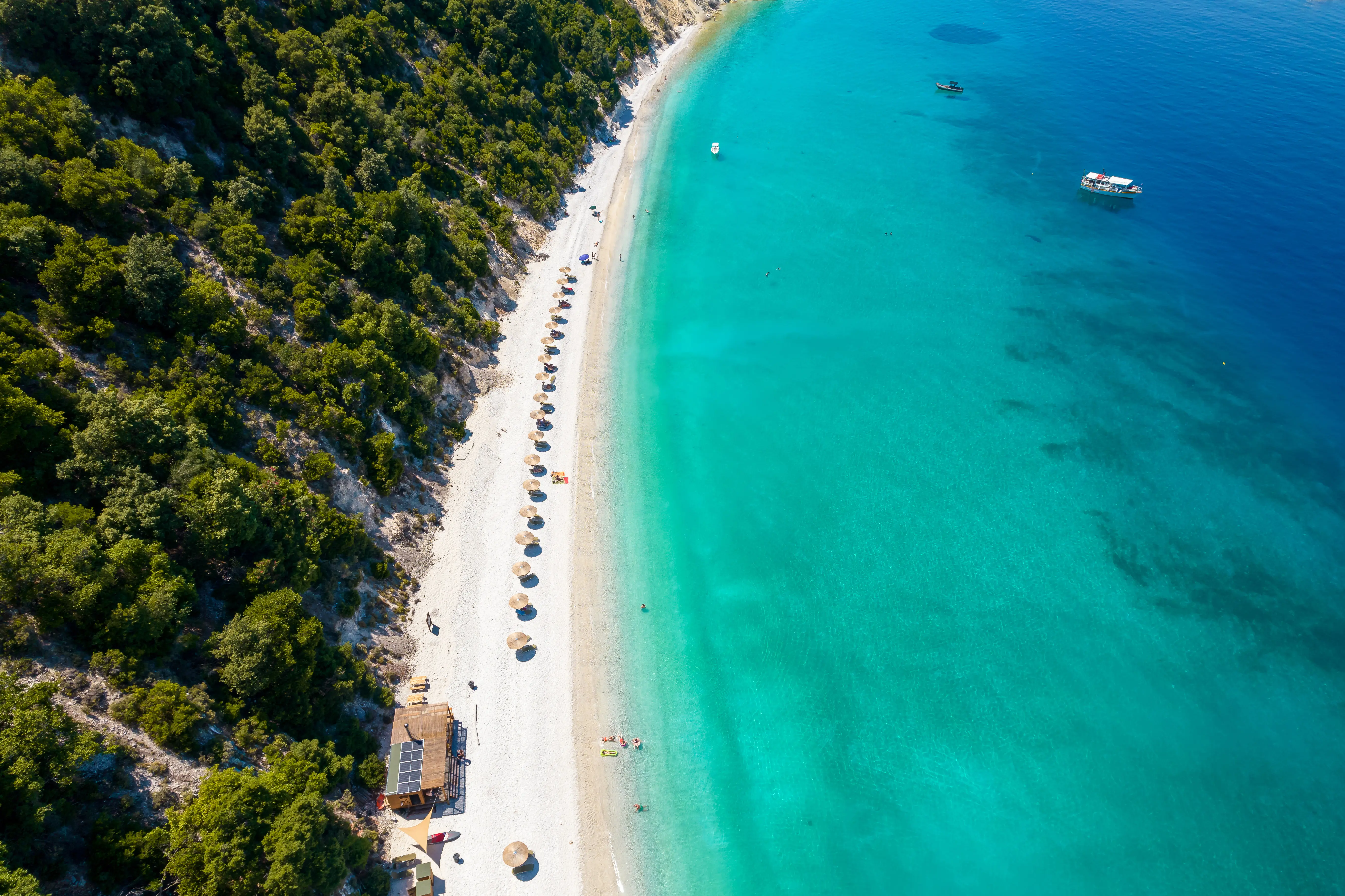 Resa till Thassos - Flygbild över idyllisk strand med kristallklart vatten och parasoller vid skogsområde.