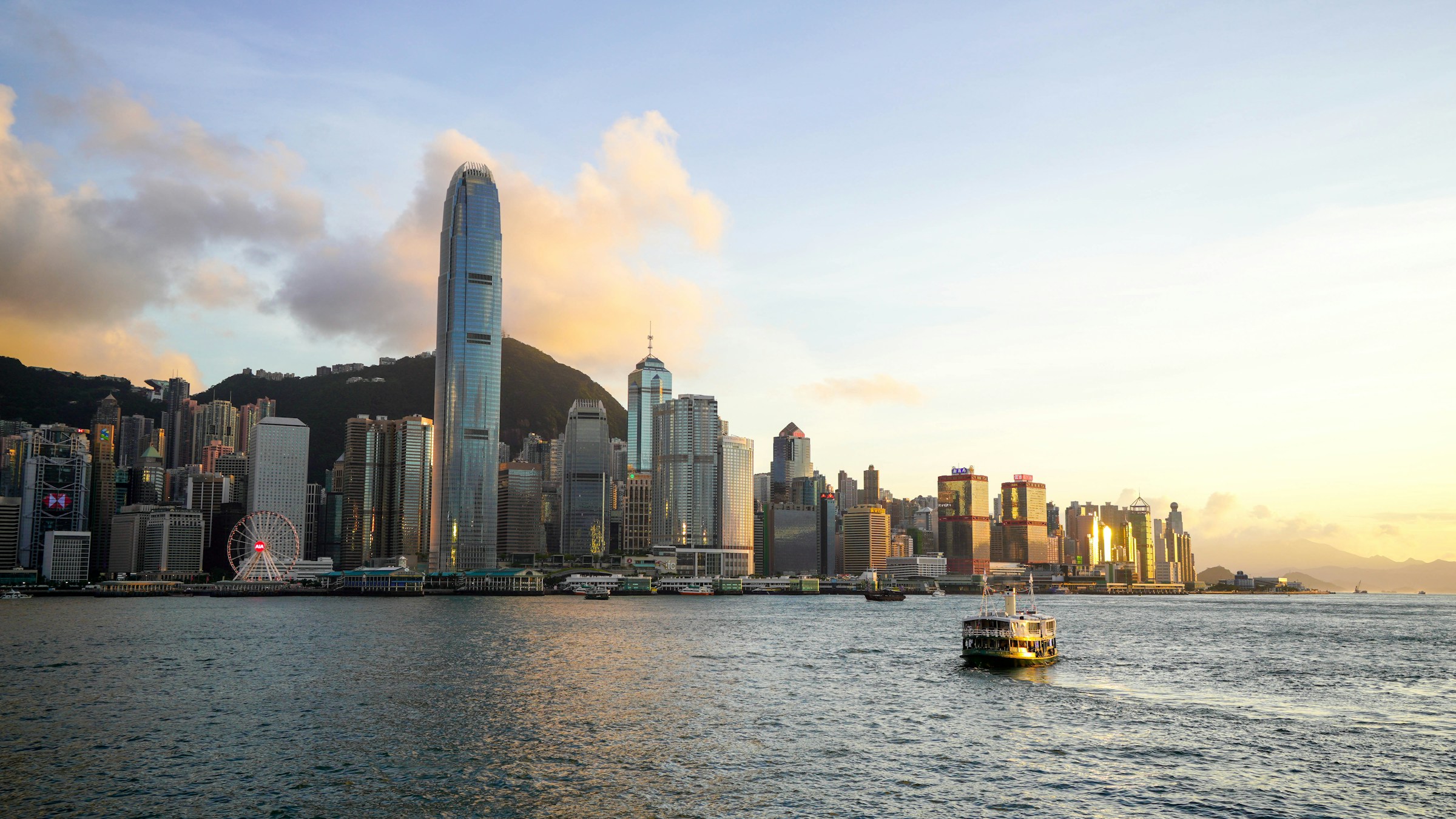 Solnedgång över Hongkongs stadssilhuett med skyskrapor och en traditionell färja på vattnet i Hongkong