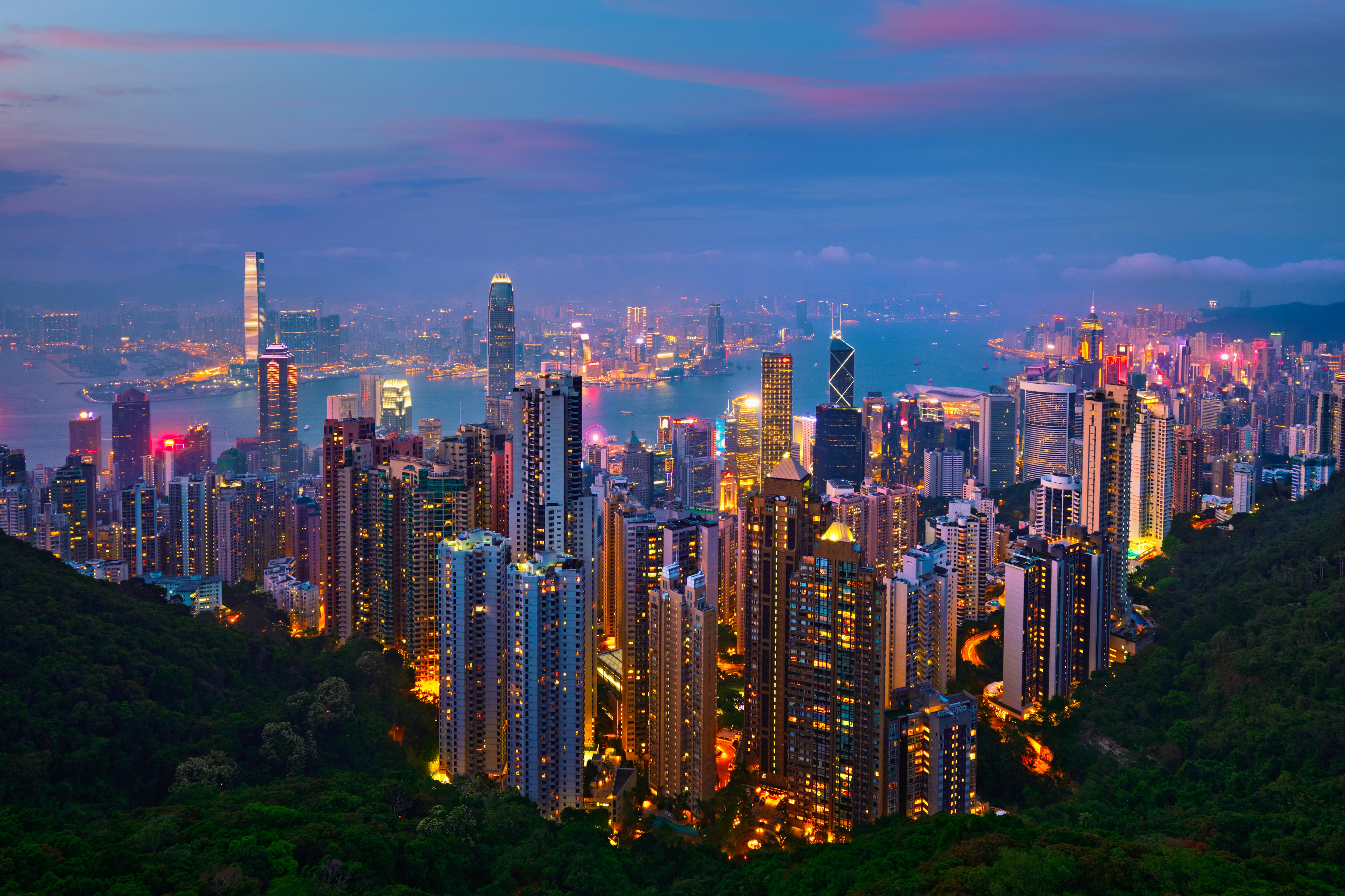 Aftonvy över en livlig HongKong skyline med upplysta skyskrapor och vatten i bakgrunden.