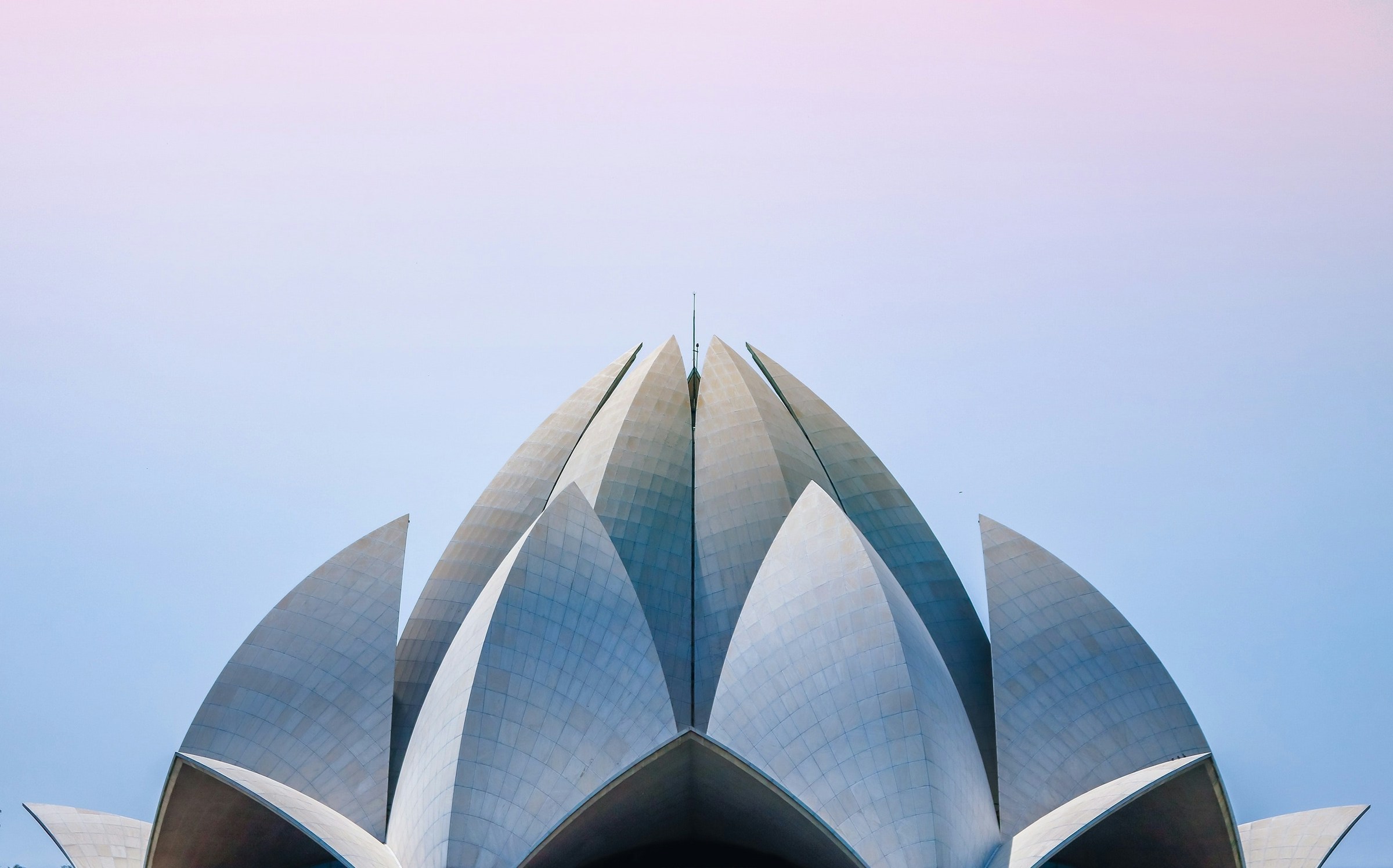 Symmetrisk vy av en modern byggnad med lotusliknande struktur mot en pastellfärgad himmel i Delhi.