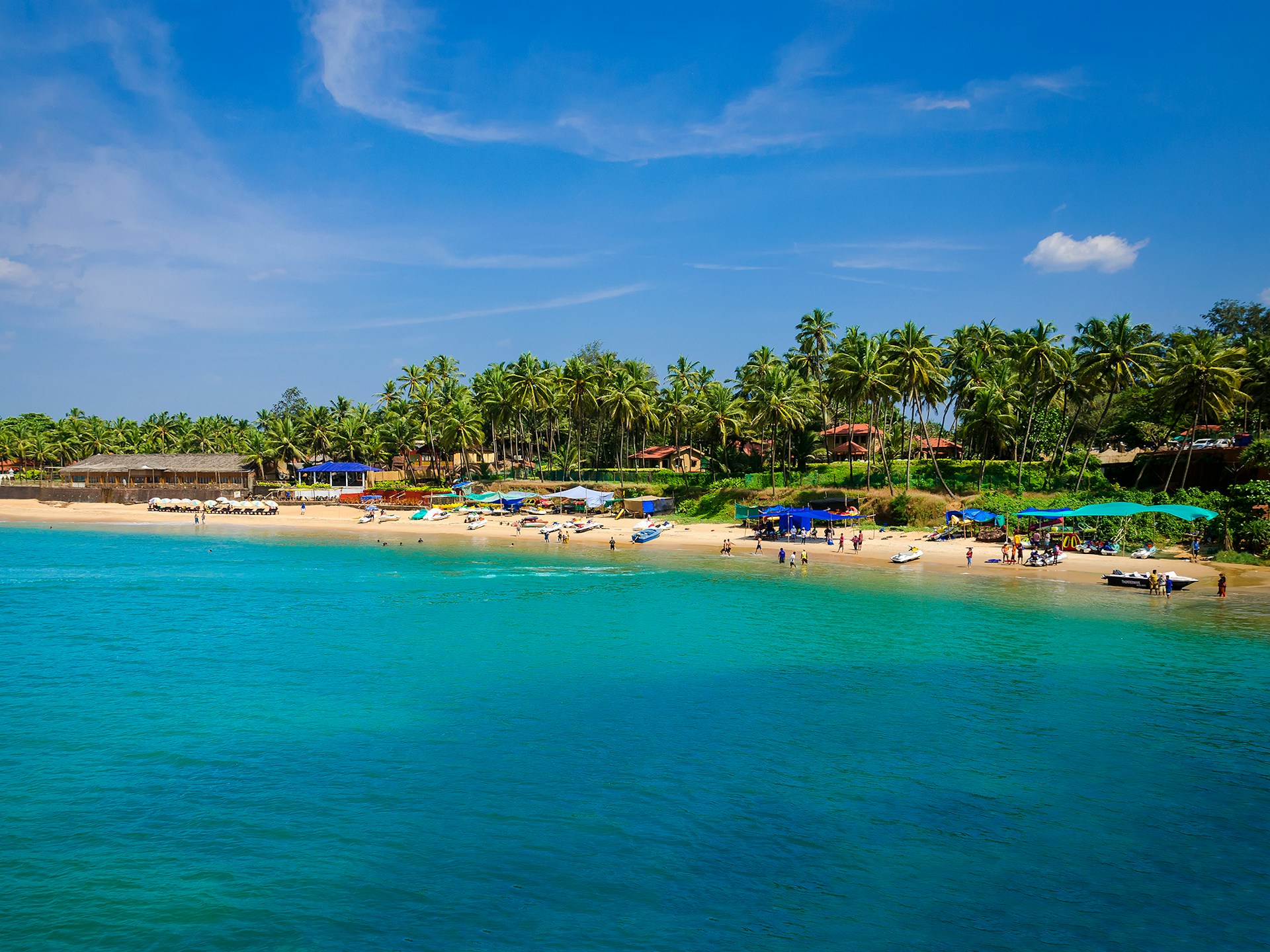 Tropisk strand med klarblått vatten och frodig grönska i Goa, full av semesterfirare och parasoller.