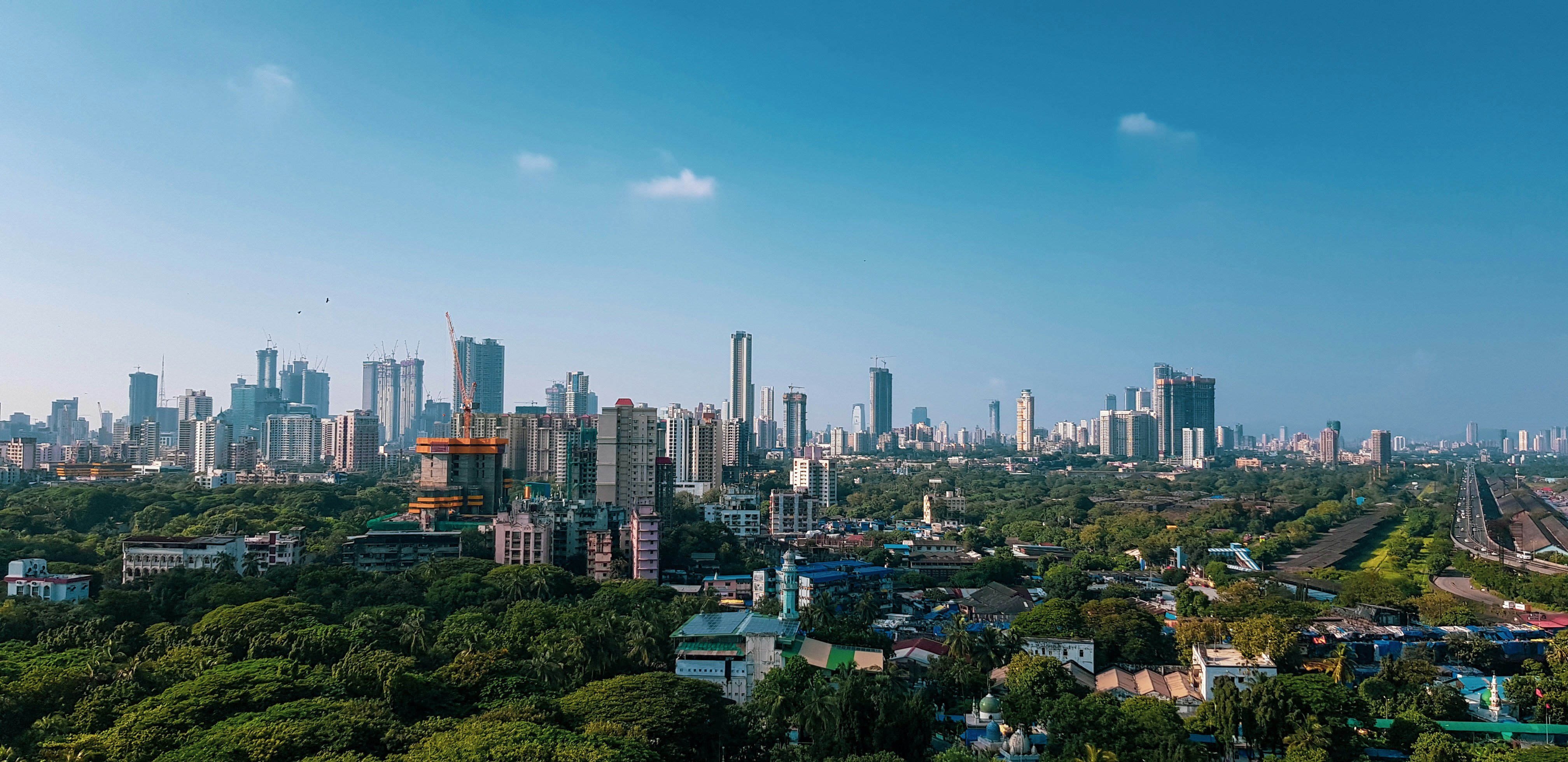 Travel to Mumbai-Bombay - Panoramic view of Mumbai with skyscrapers, green parklands, and a clear blue sky.