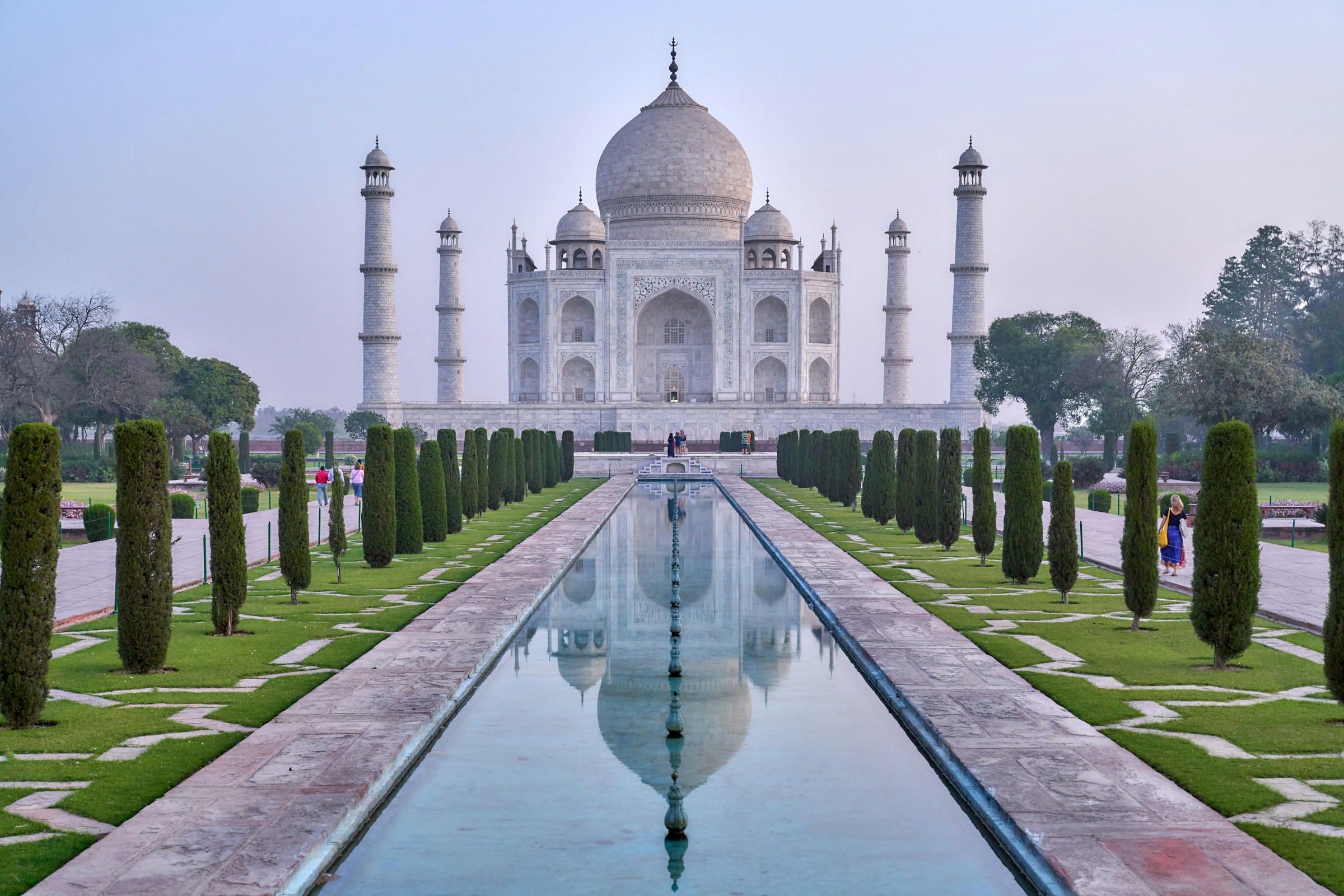 Taj Mahal i Indien vid gryningen med reflekterande vatten och prydliga häckar.