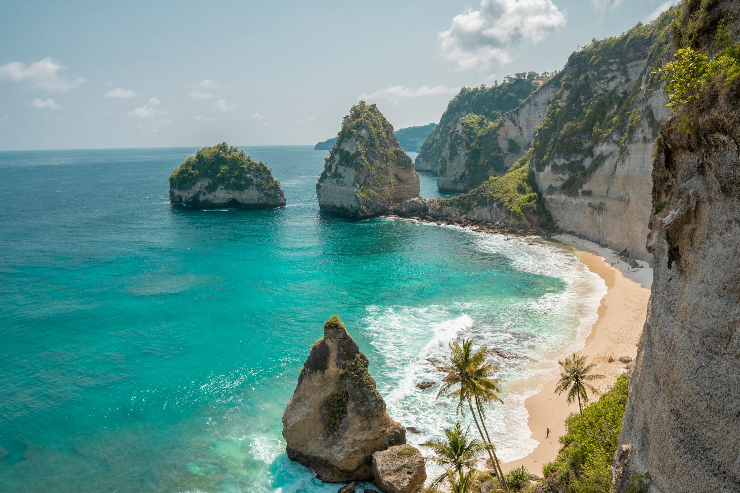 Vacker strand med blått hav möter höga klippor med palmer och grönska i Bali