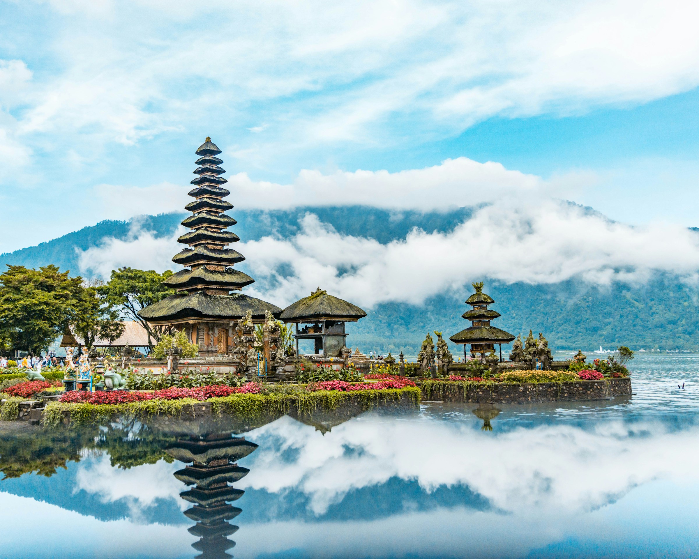 Vackert tempel i Bali vid en sjö omgiven av grönska och blå himmel i bakgrunden