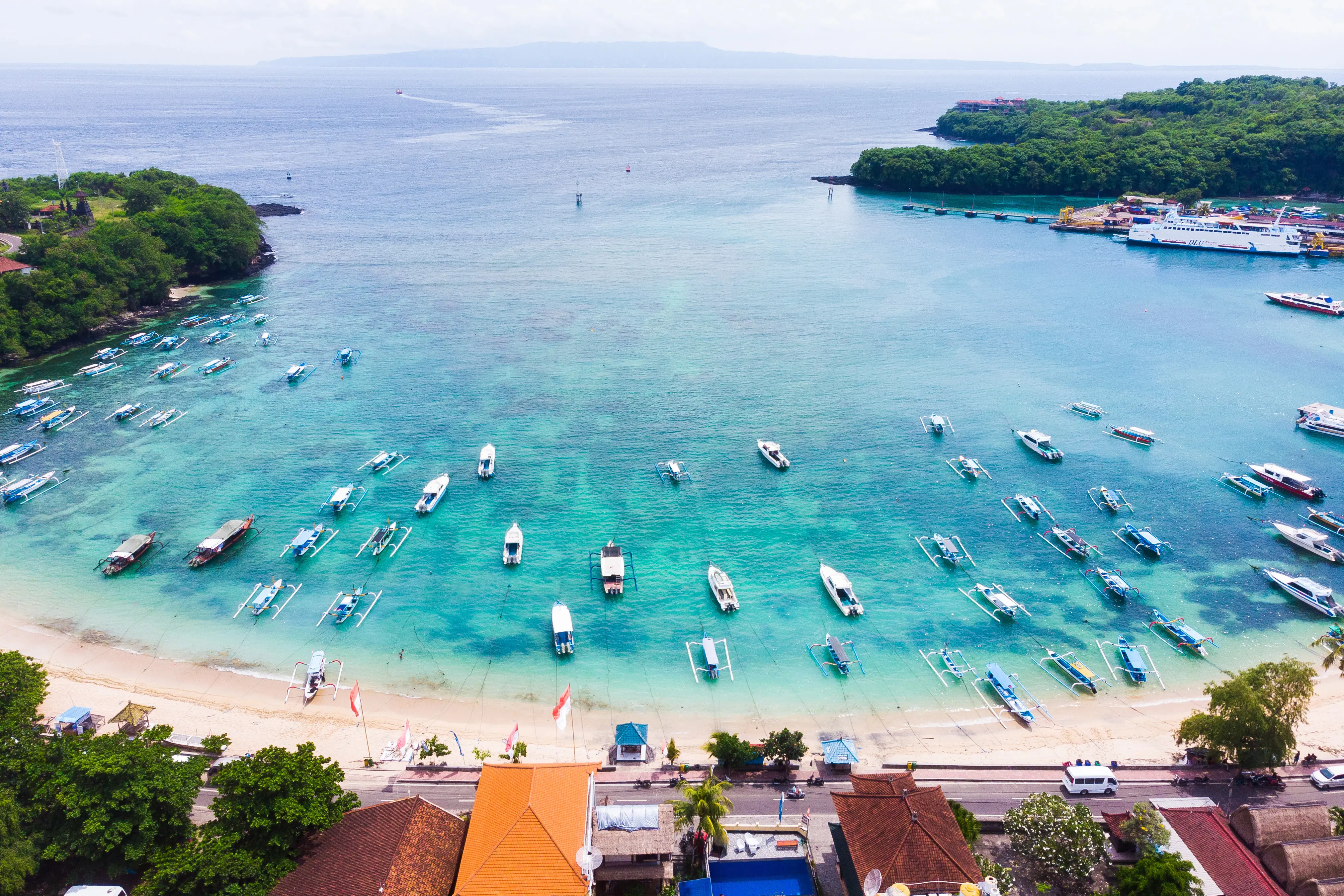 Resa till Indonesien - Vy över strand och blått hav i en bukt med båtar i Indonesien