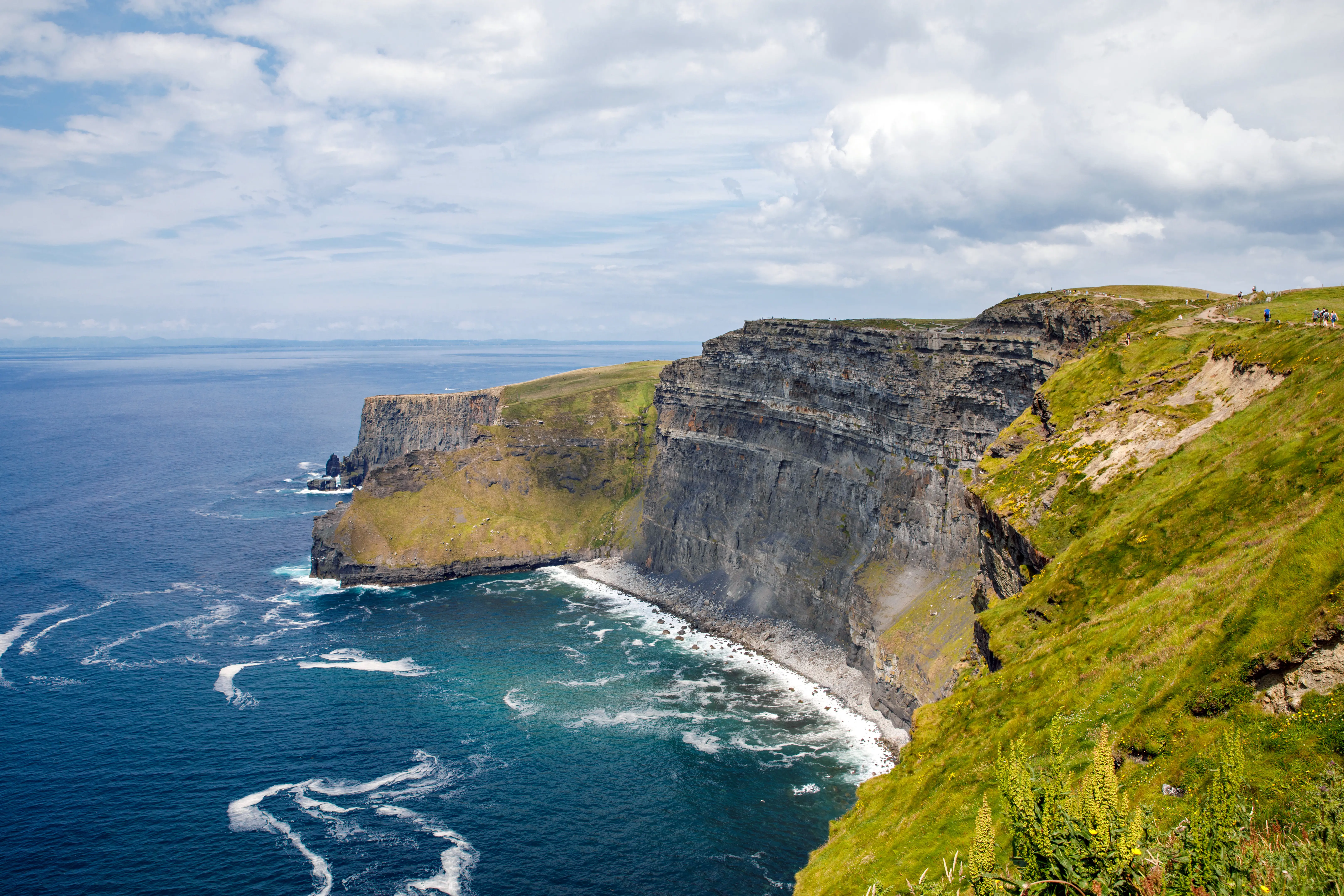 Resa till Irland - Majestätiska klippformationer vid havet med grönt gräs och klart blå himmel på Klipporna av Moher.