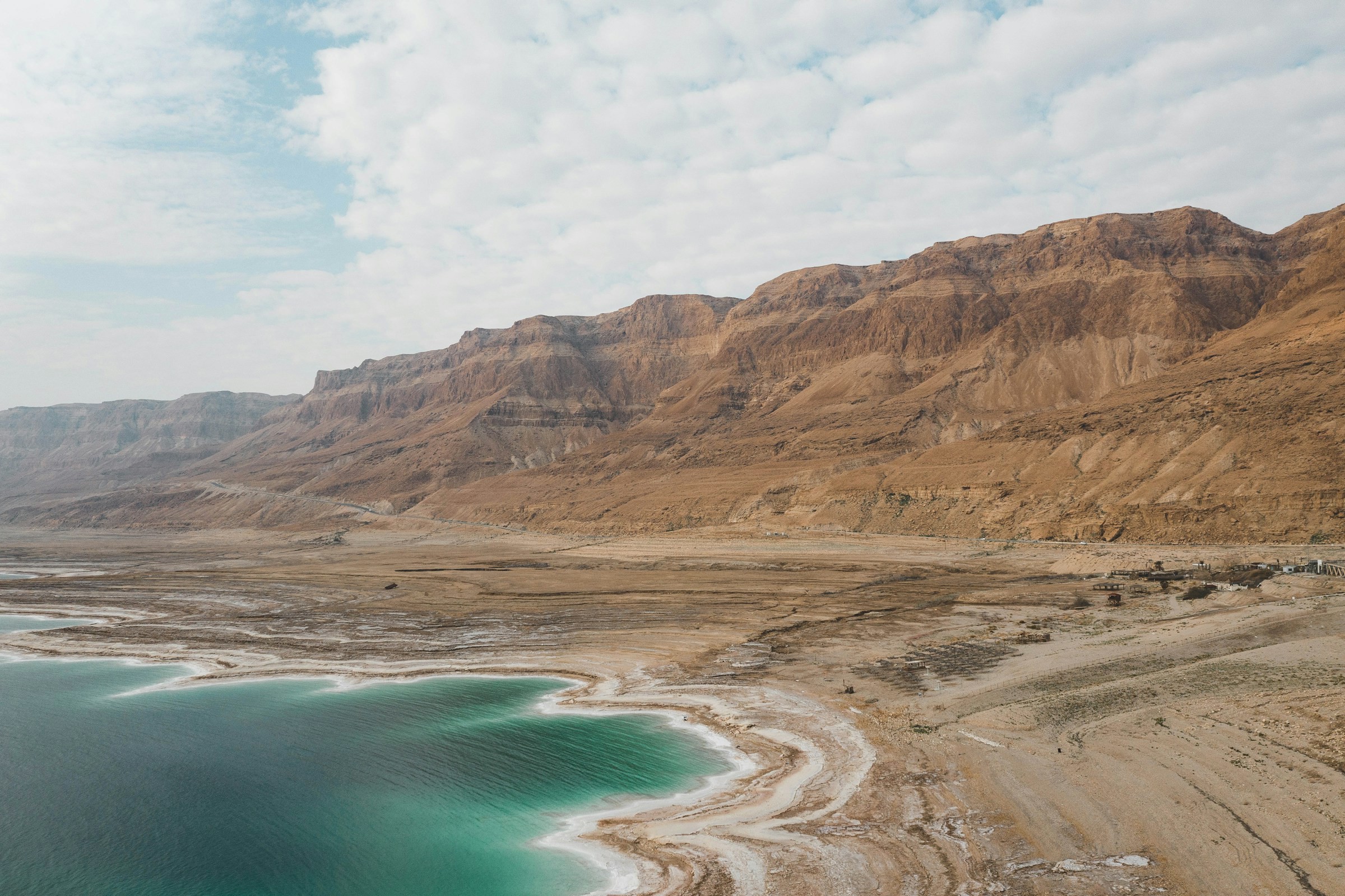 Vy över döda havet som möter en öde strand och stora klippor mot molnig himmel i Israel