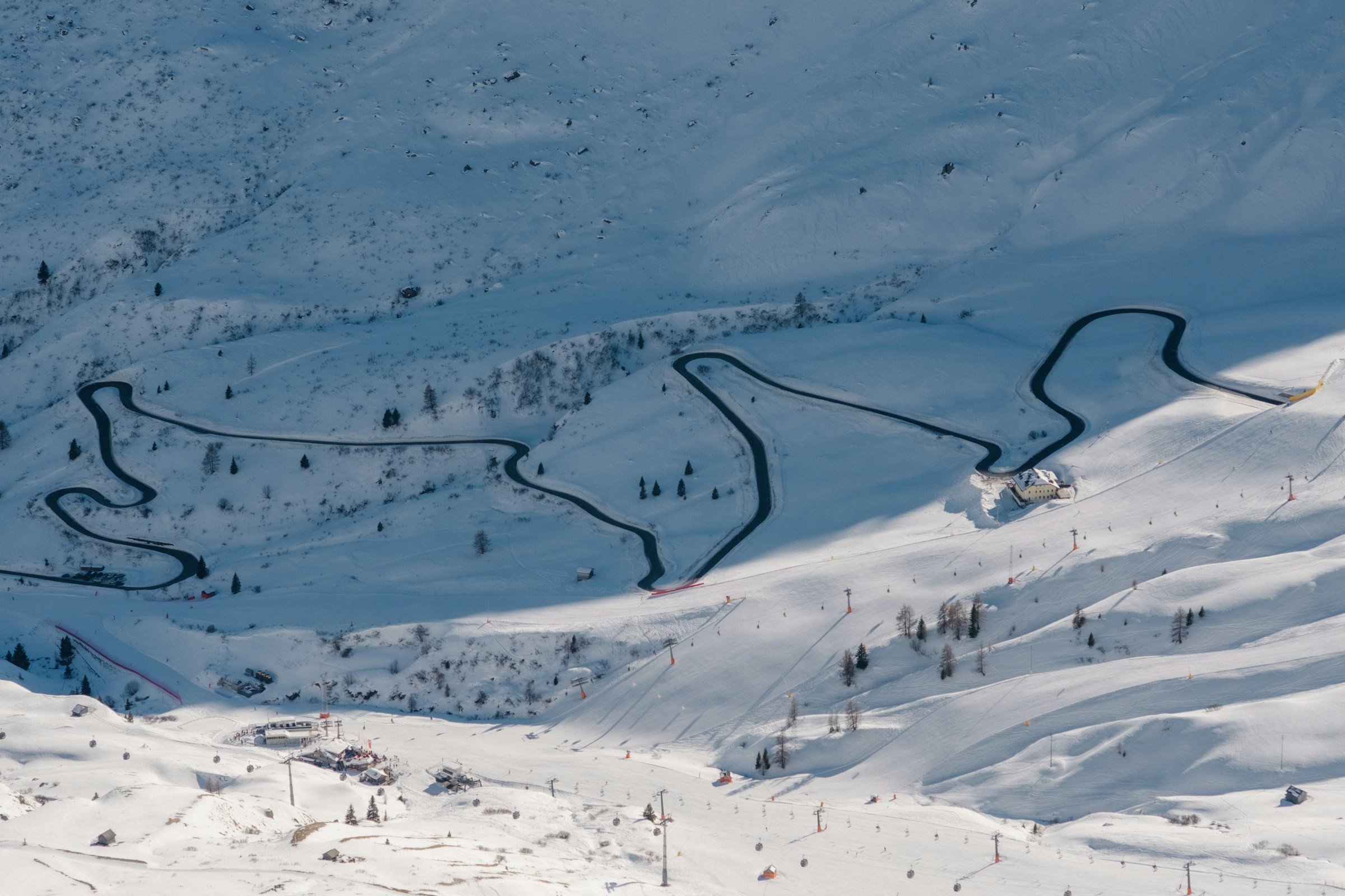 View down from a snow-covered ski slope towards a ski resort with roads between the valleys