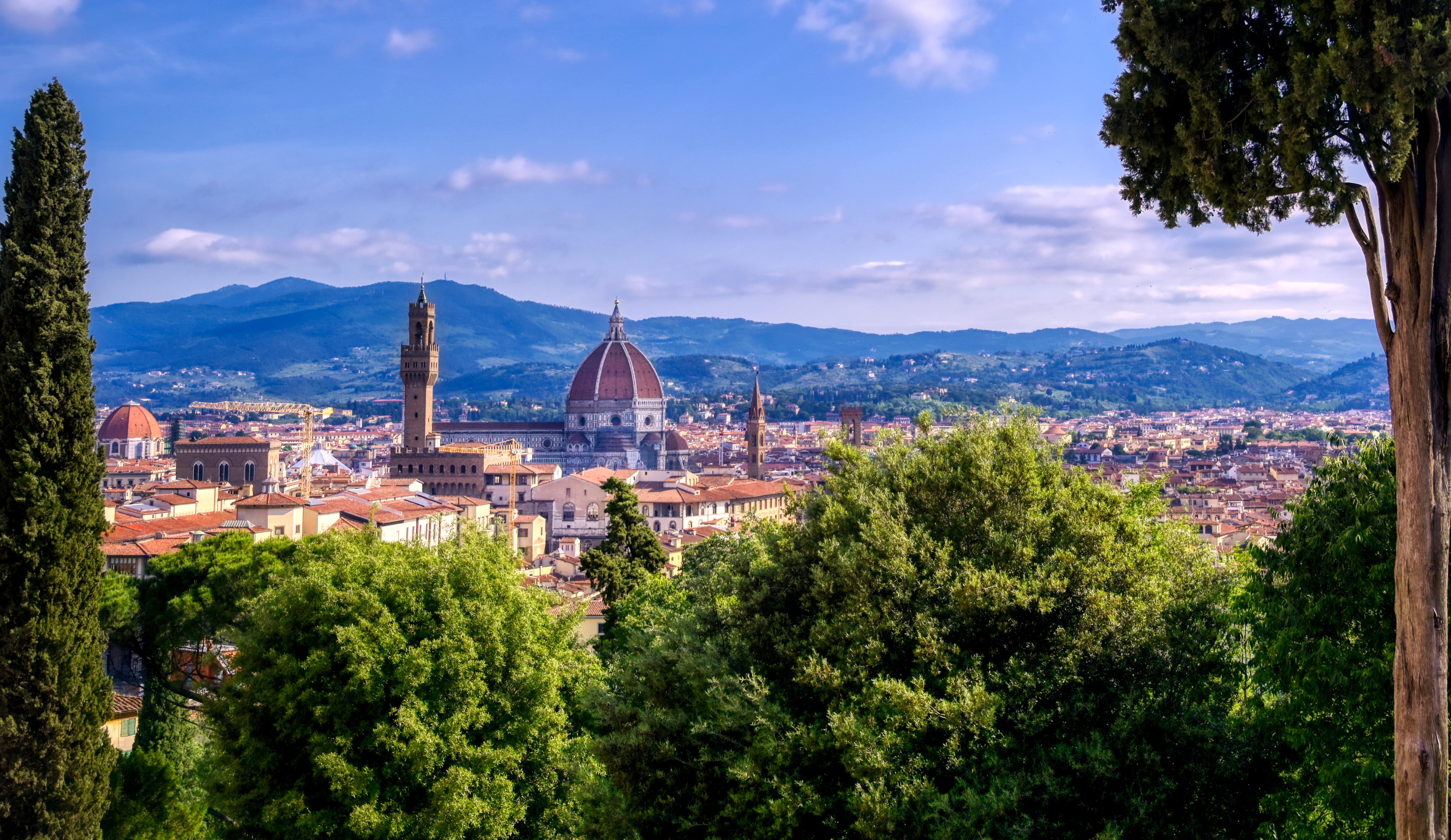 Travel to Florence - View from a height over Florence in Italy where lush trees meet city with famous church and blue sky in the background