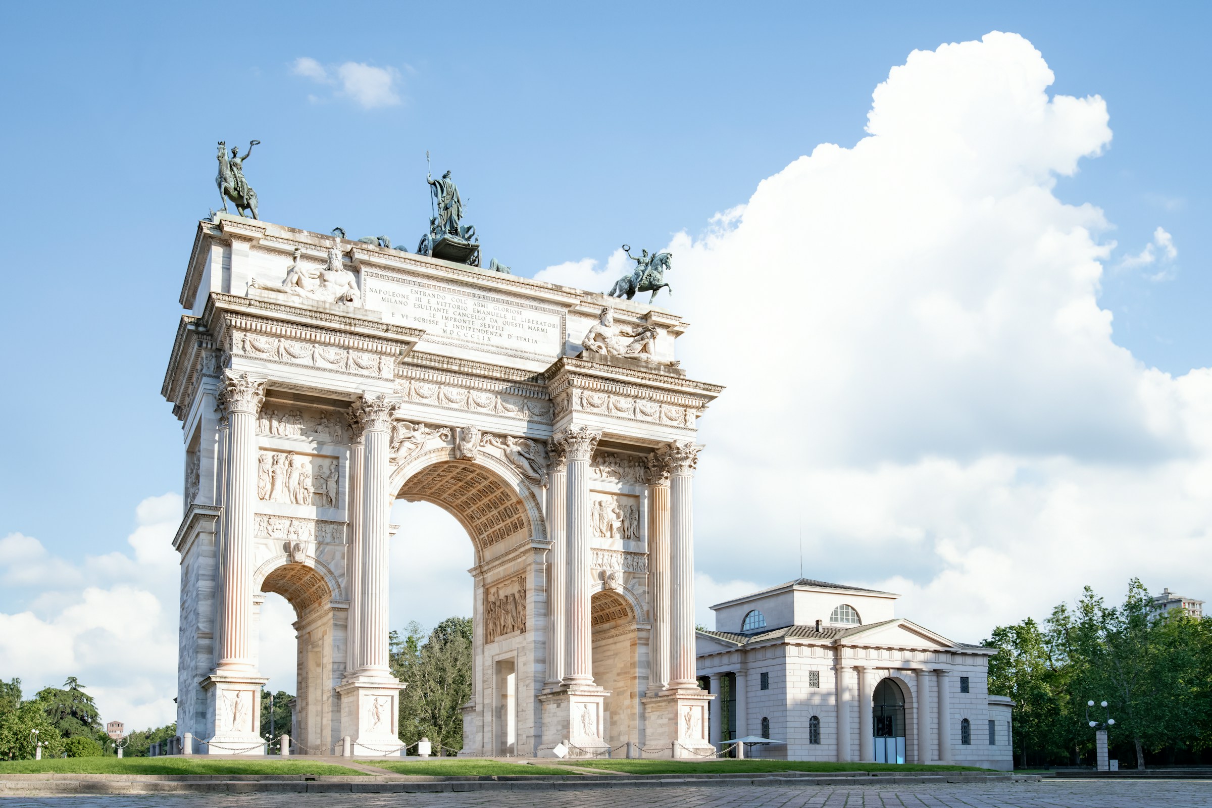 Triumfbåge med skulpturer mot en klar himmel, arkitektoniskt landmärke och historiska monumentet i Milano.