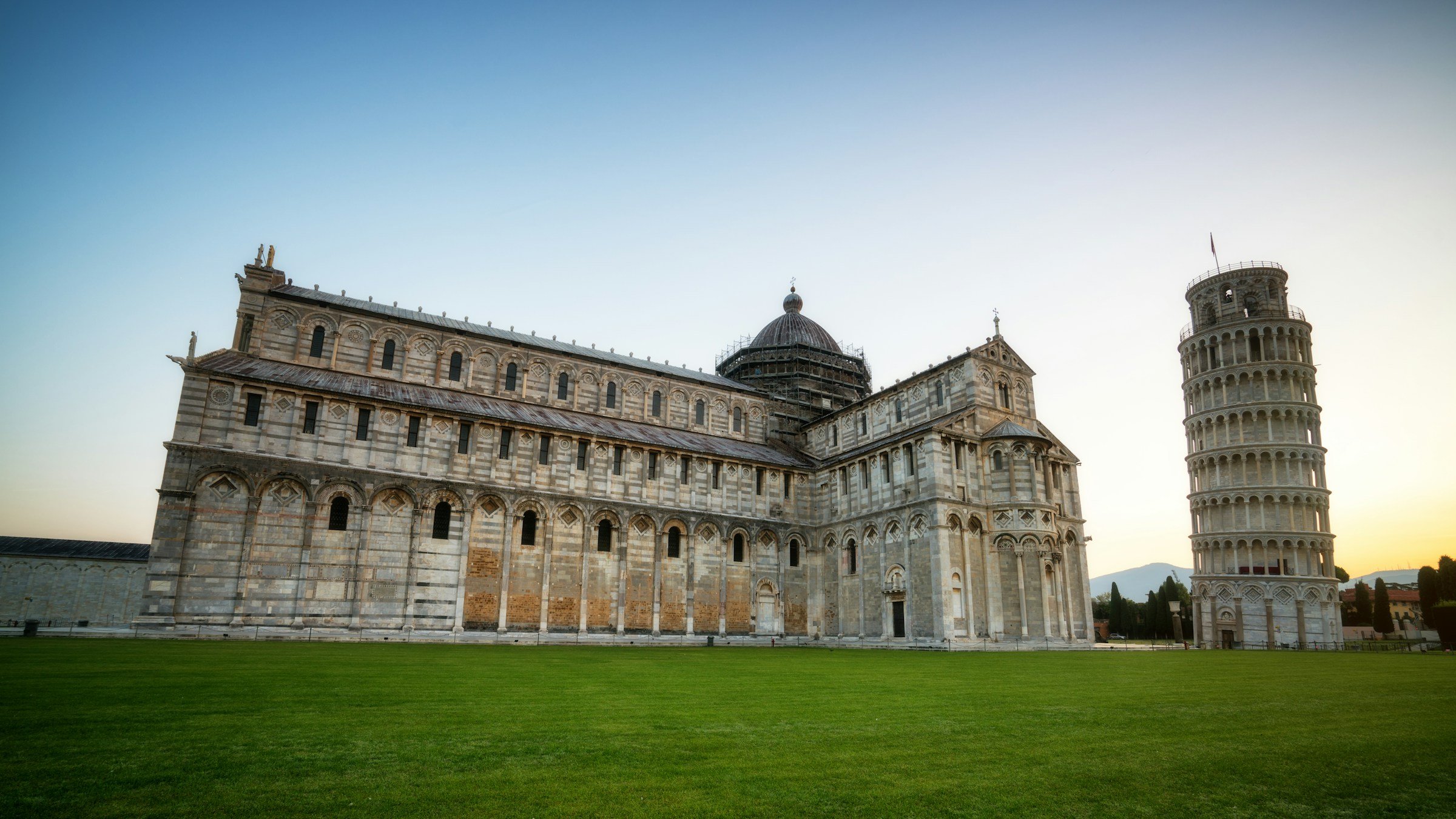 Beautiful traditional Italian white building on a lawn with leaning tower of Pisa next to it