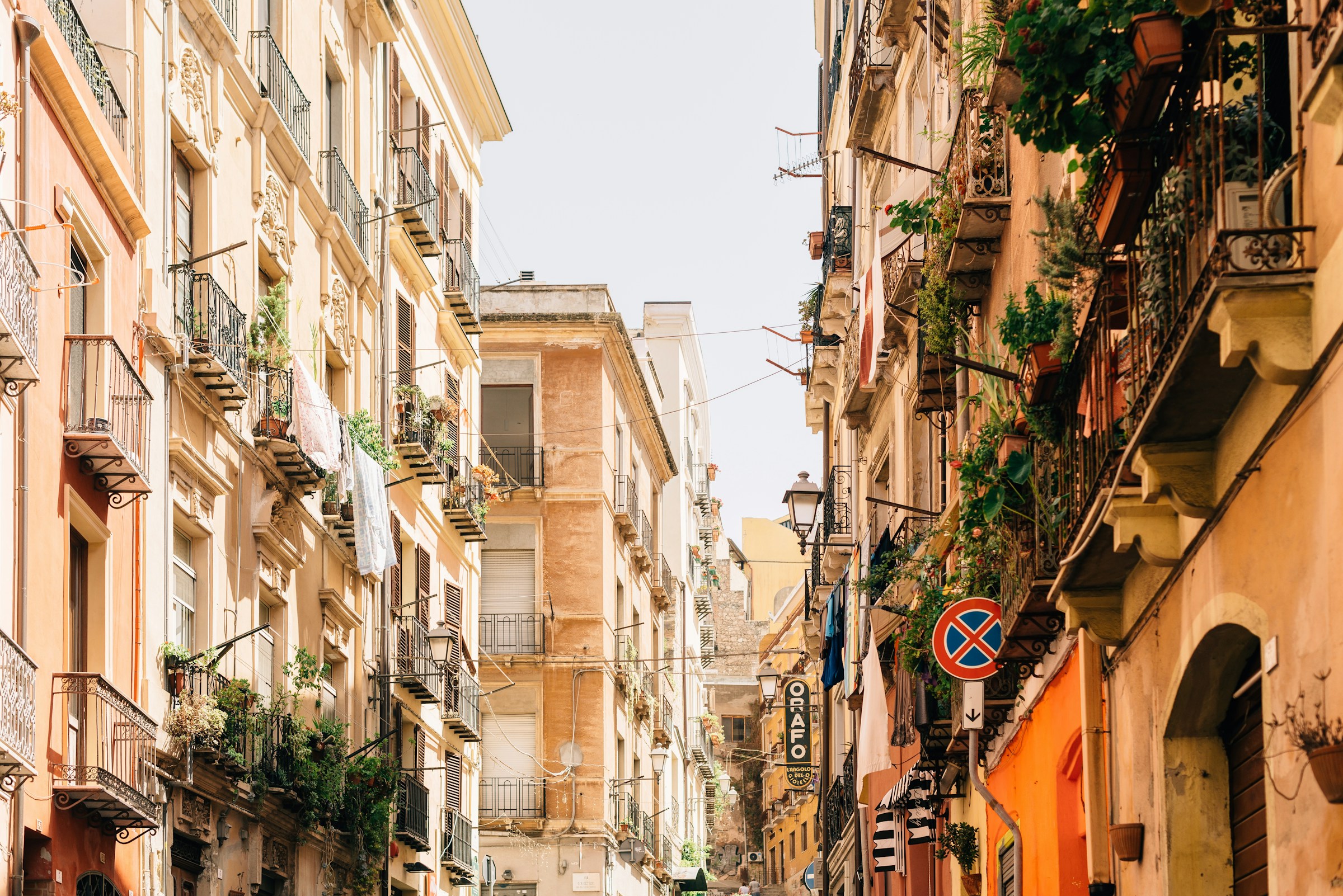 Pittoresk gata med traditionella byggnader och balkonger i en medelhavsstad, dekorerad med växter och torkande tvätt på Sardinien.