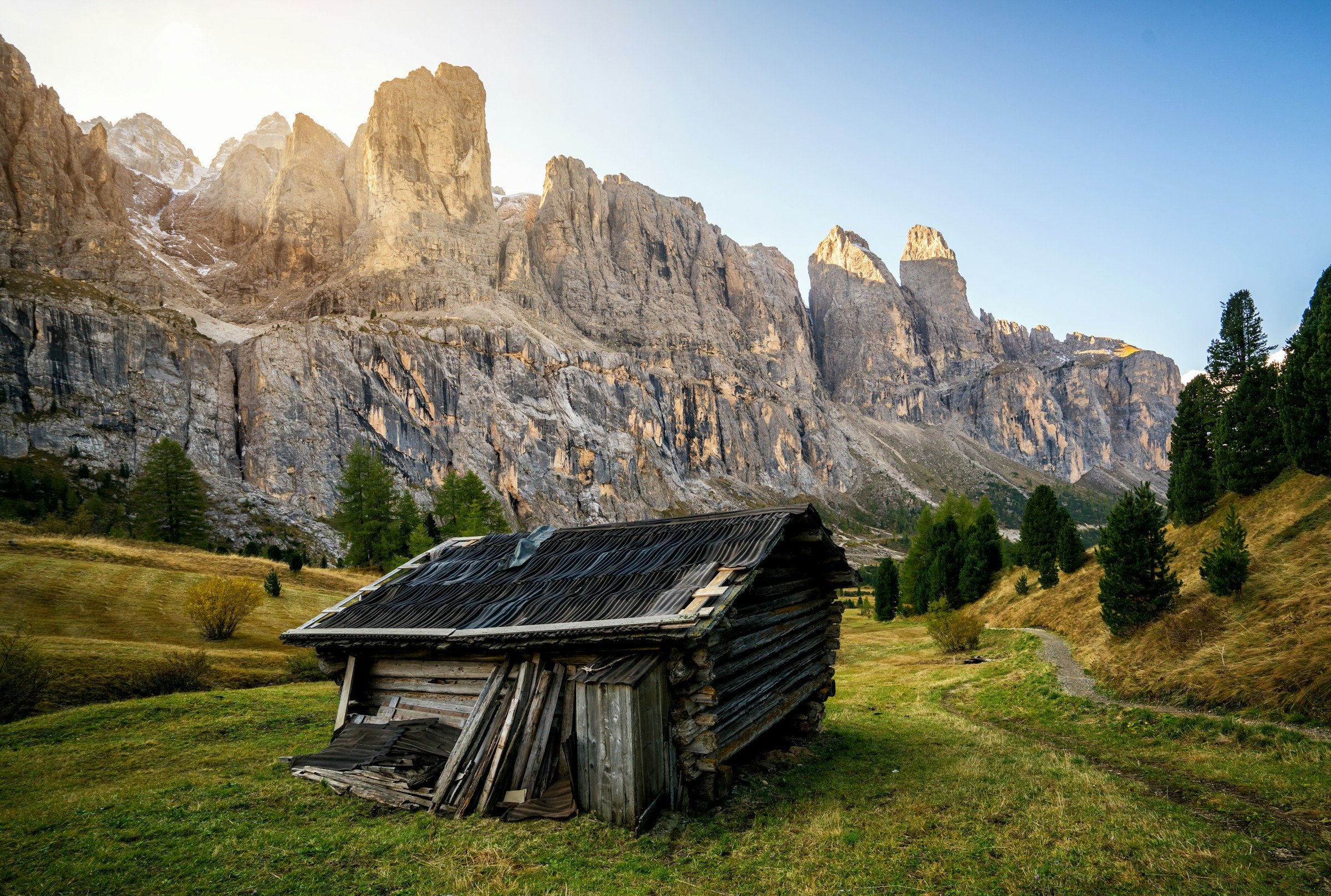 A lonely cottage stands in a green valley between mighty cliffs in Val Gardena with a sunrise in the background