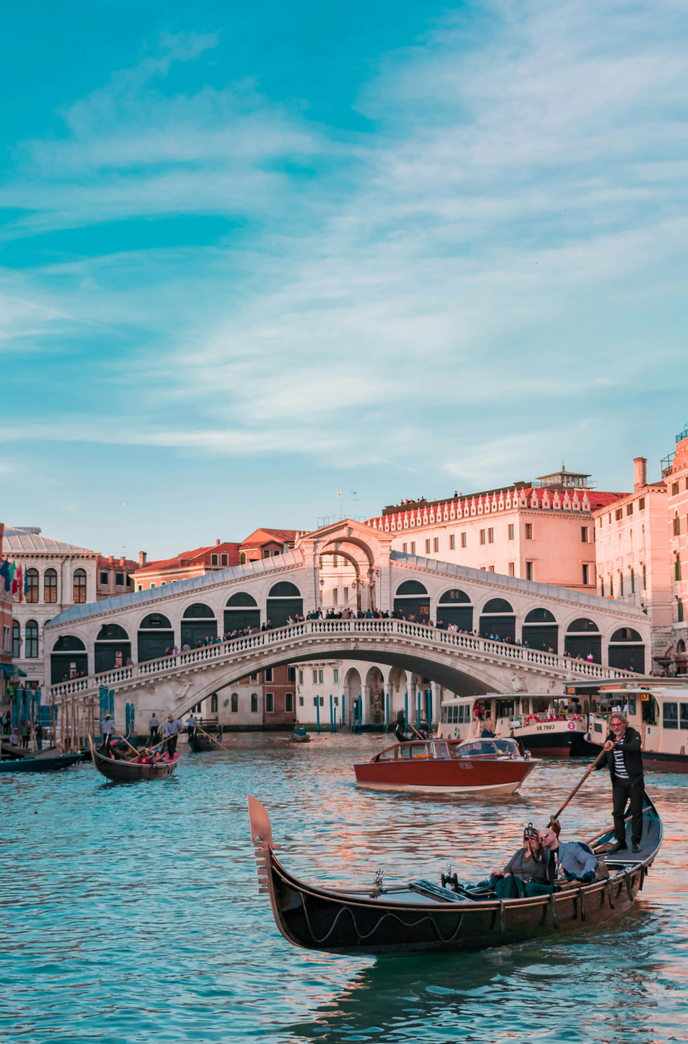 Gondol framför den berömda Rialtobron i Venedig med blå himmel i bakgrunden."