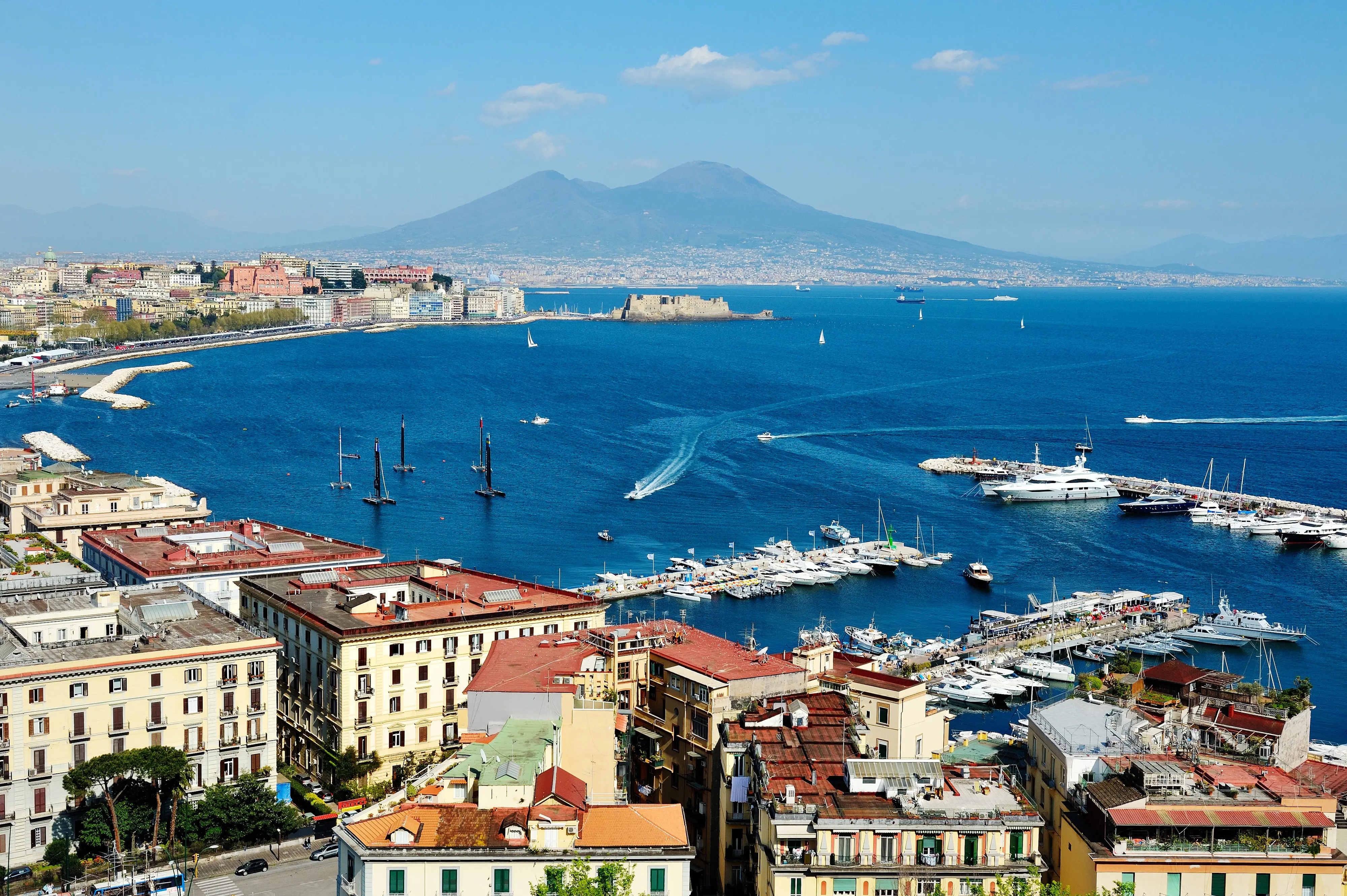 Resa till Neapel - Vy över Neapelbukten med Vesuvius i bakgrunden, båtar och fartyg på det glittrande havet och klassisk arkitektur i förgrunden.