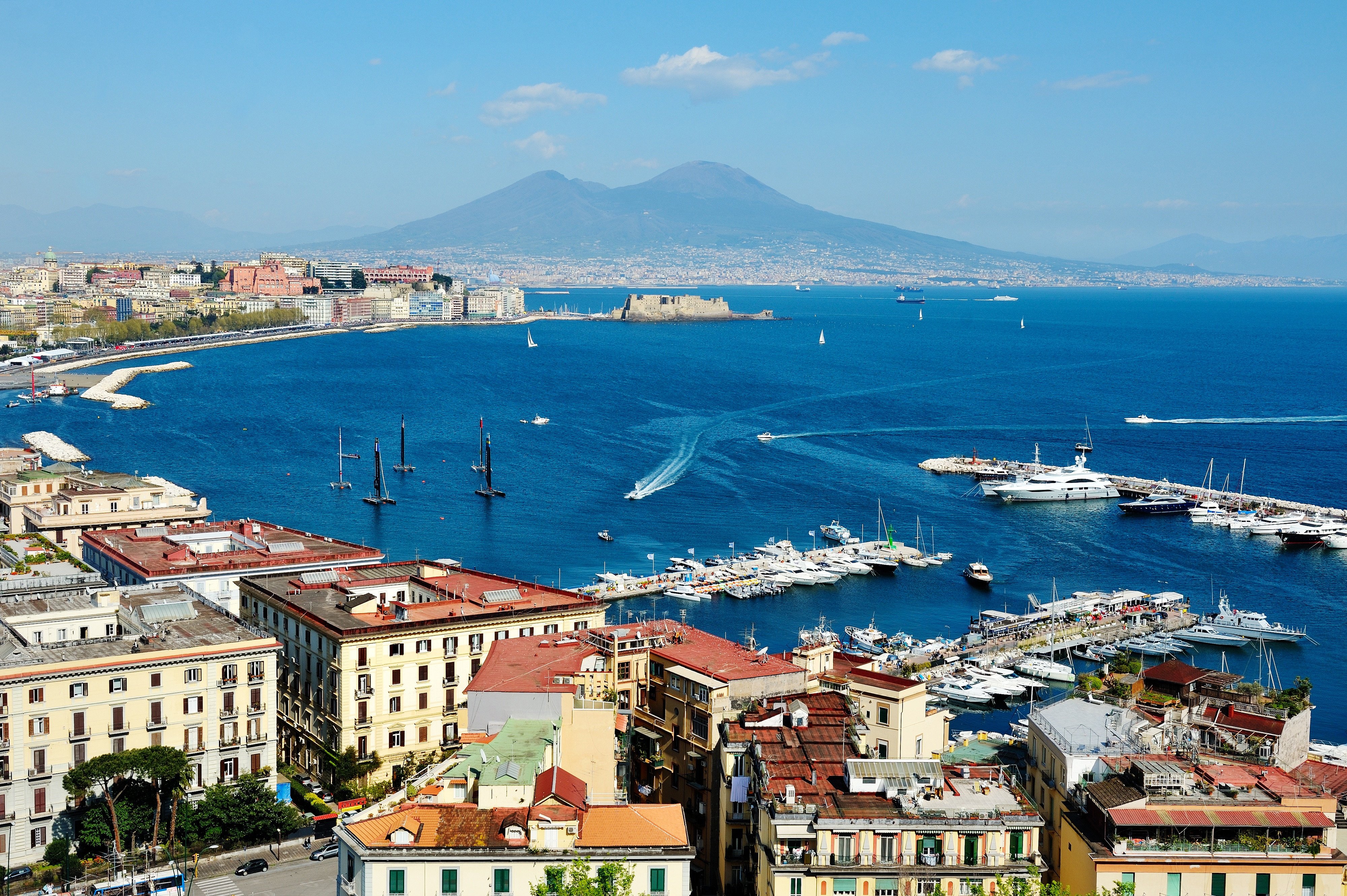 Resa till Neapel - Vy över Neapelbukten med Vesuvius i bakgrunden, båtar och fartyg på det glittrande havet och klassisk arkitektur i förgrunden.