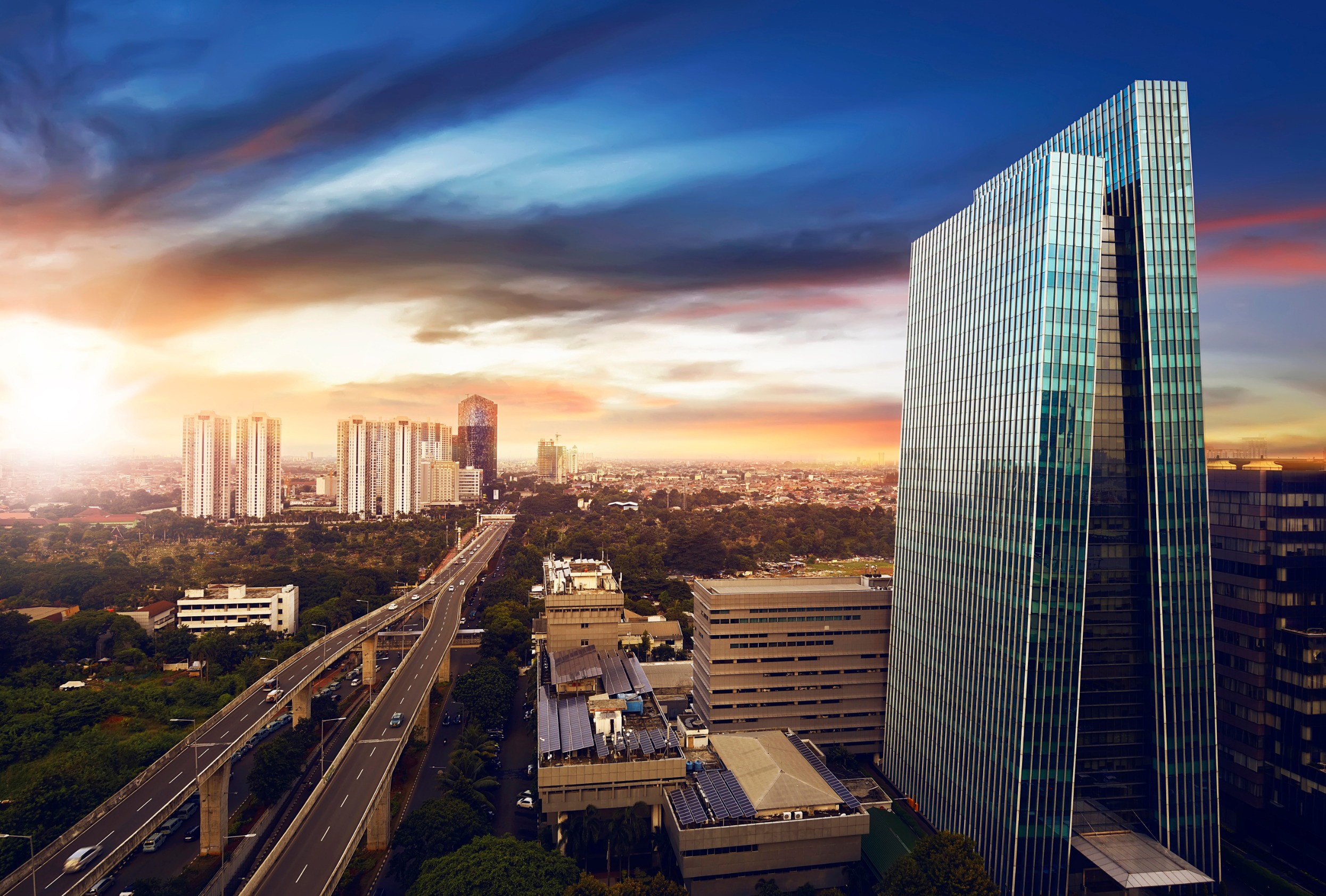 Solnedång över Jakarta-stad med en motorväg och skyskrapa i glas med stadssilhouette i bakgrunden