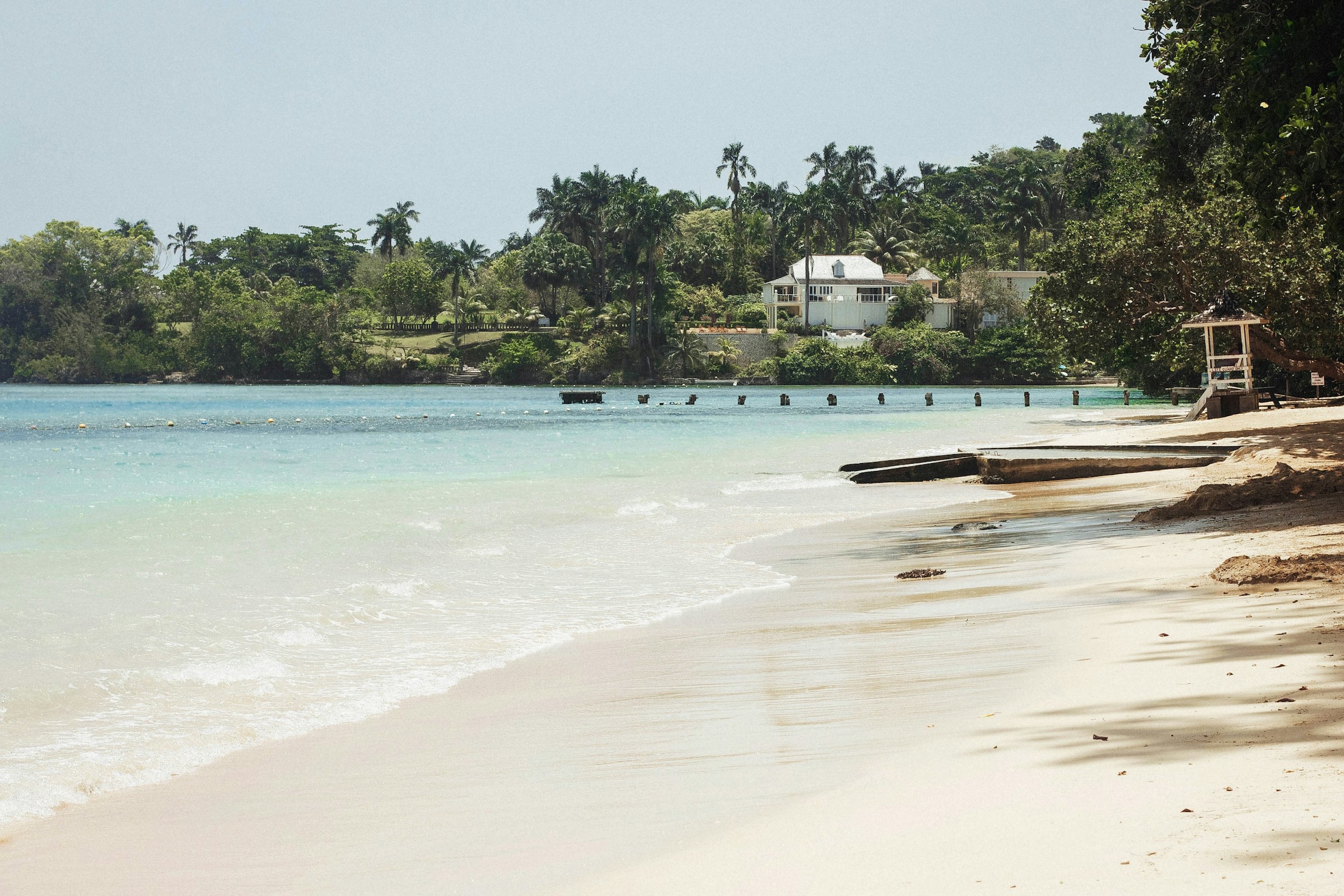 Vacker vit strand möter turkosblått vatten vid djungel och ett hotell i bakgrunden på Jamaica