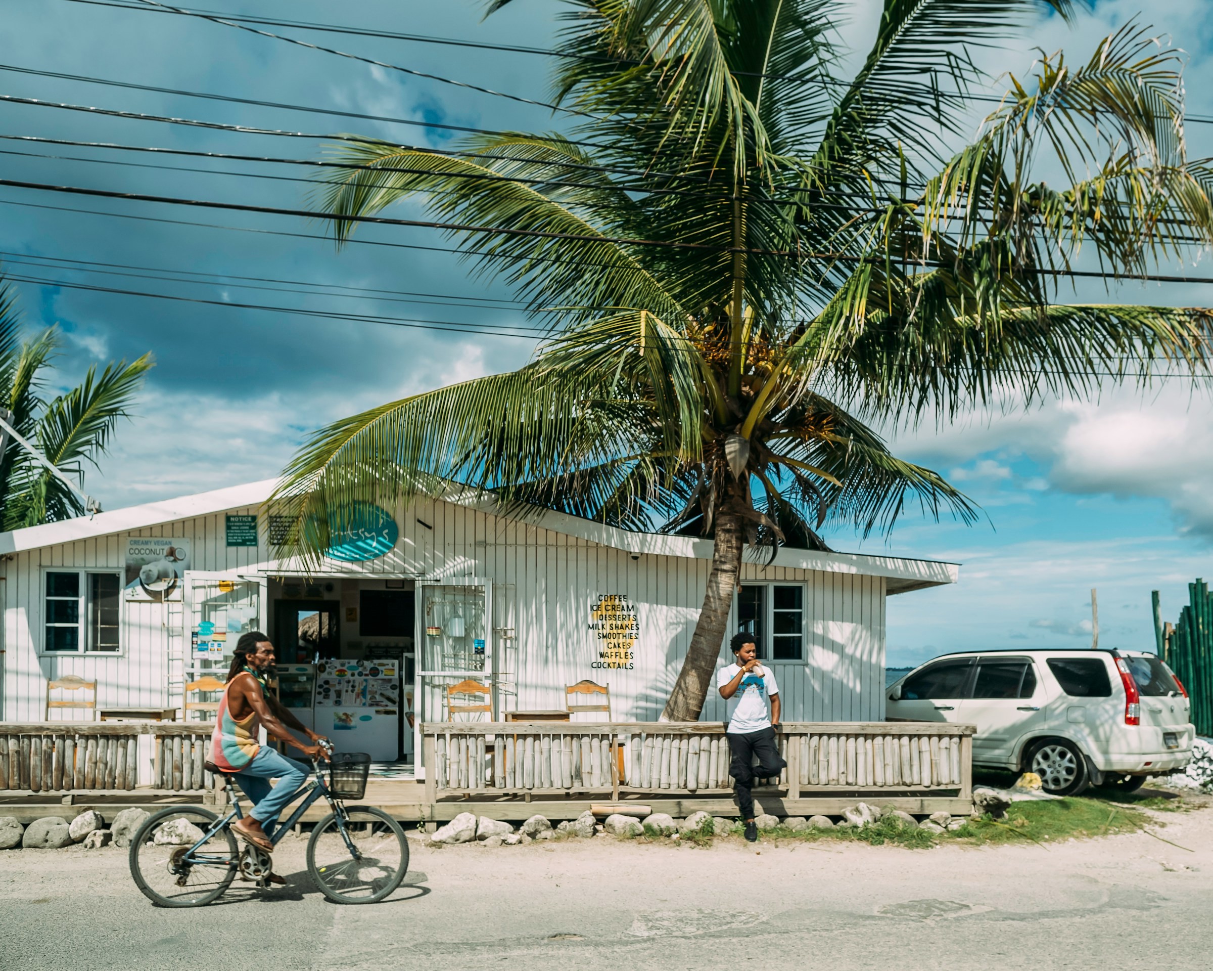 Liten butik vid sidan av en väg med ett palmträd och en man på cykel på Jamaica