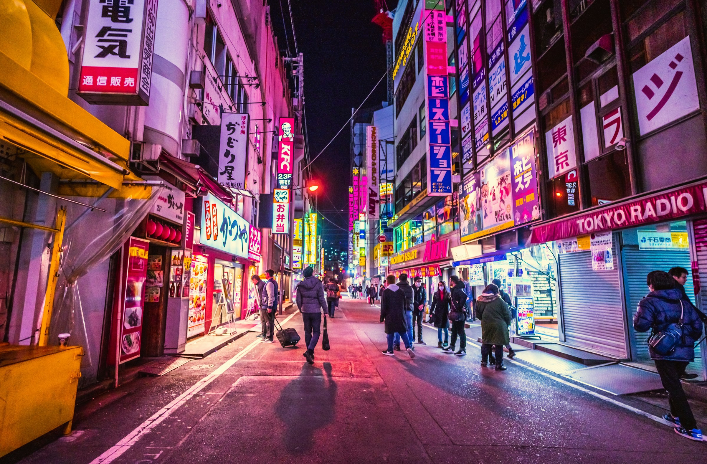 Gata i Tokyo med neon skyltar som lyser upp alla fönster i rosa ljus med folk som går