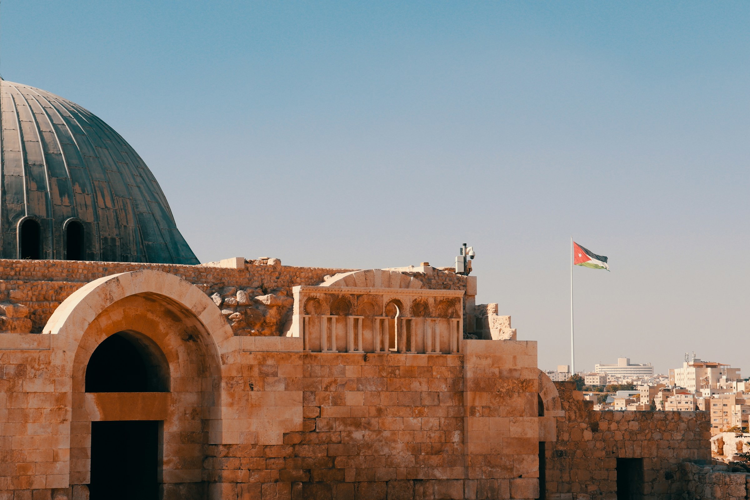 Vy över vacker msoké med en stad i bakgrunden och Jordaniens flagga som svajar mot en blå himmel