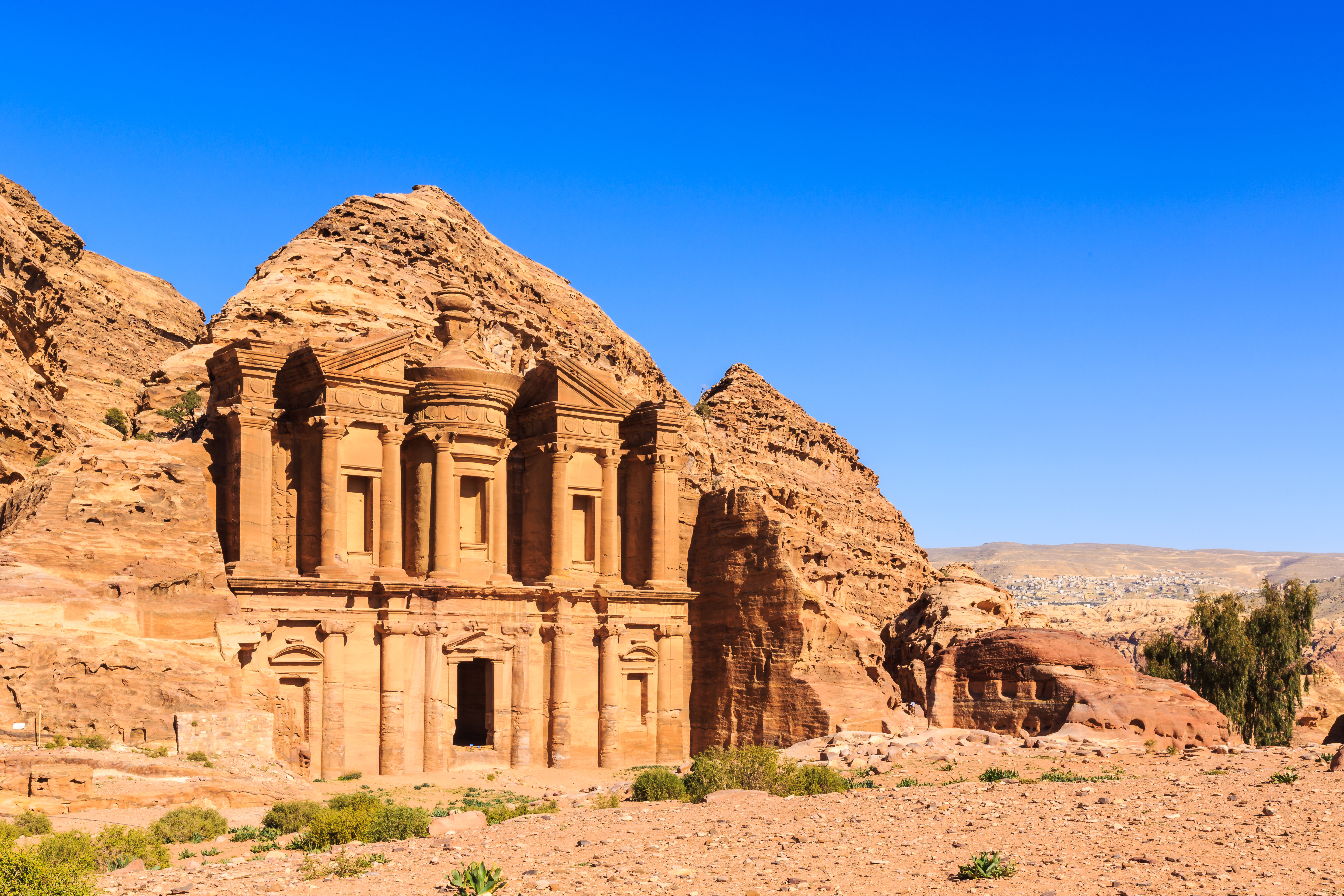 Resa till Jordanien - Det antika Ad Deir-klostret i Petra, Jordanien, inristat i rosenröd klippa under klarblå himmel.