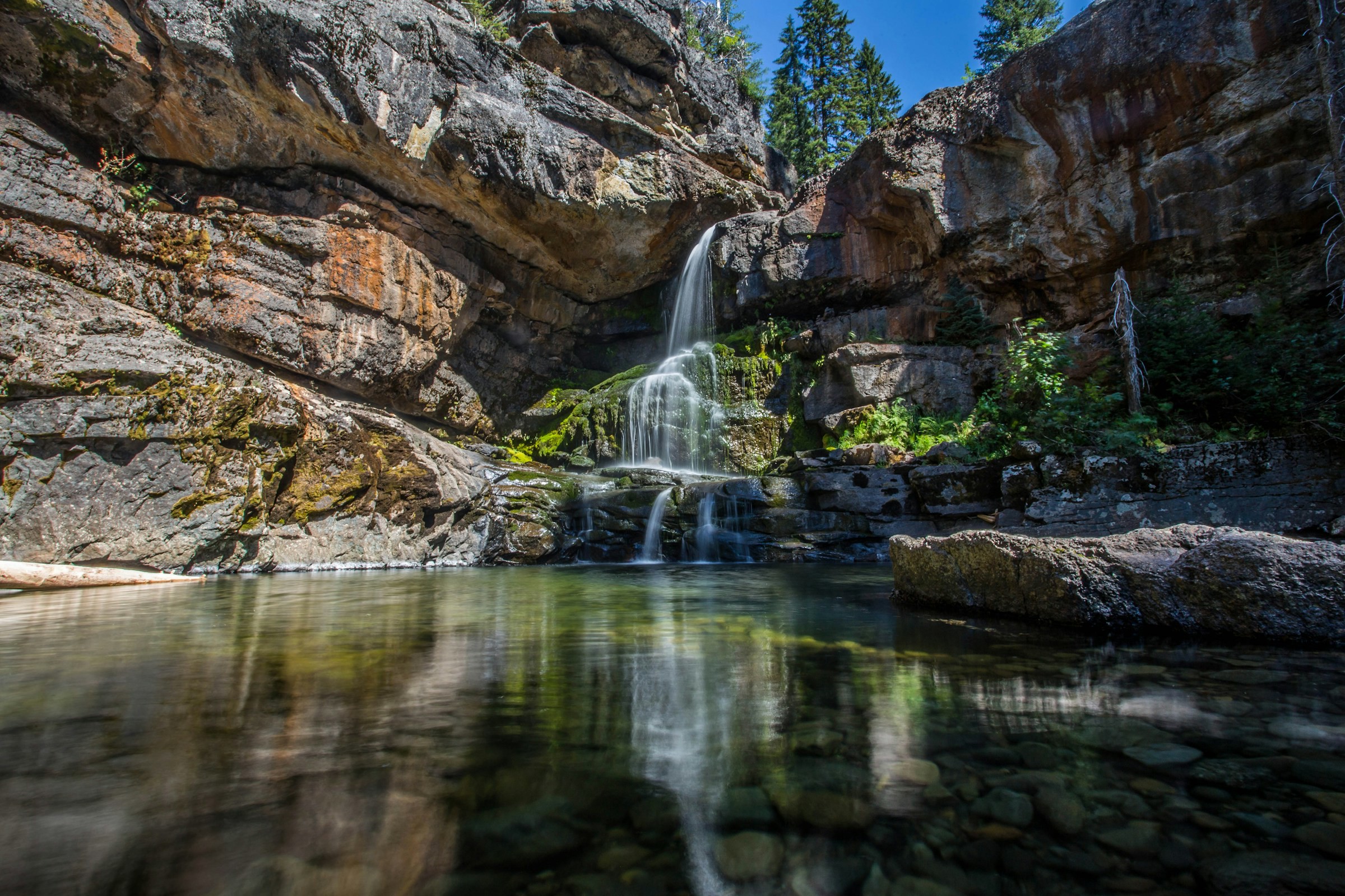 Scenic waterfall with clear waters and lush mossy rocks in a forest environment.