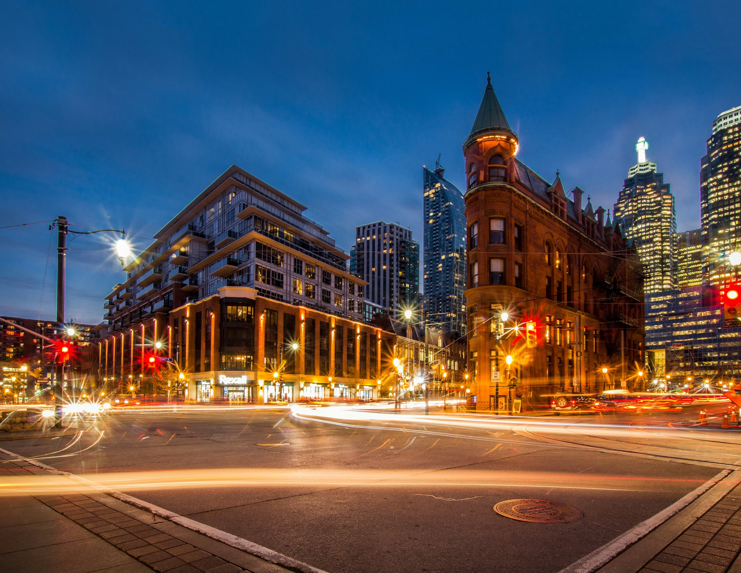 Flatiron-byggnaden i Toronto under kvällstid vid en korsning med trafik och belysning över gatorna