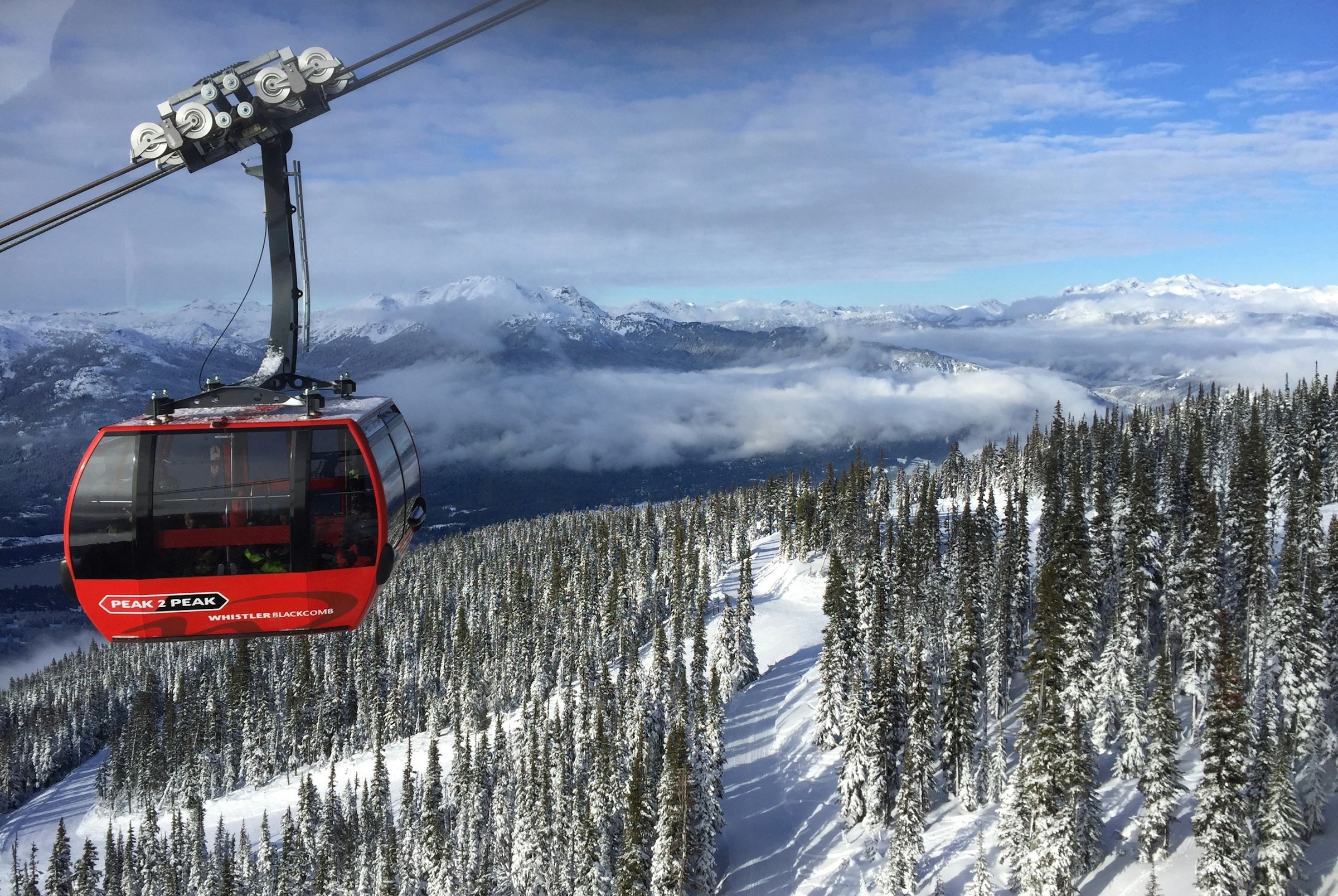 Röd gondollift mot bakgrund av snötäckta berg och skogar i Whistler Blackcomb, perfekt för skidåkning och bergsturism.