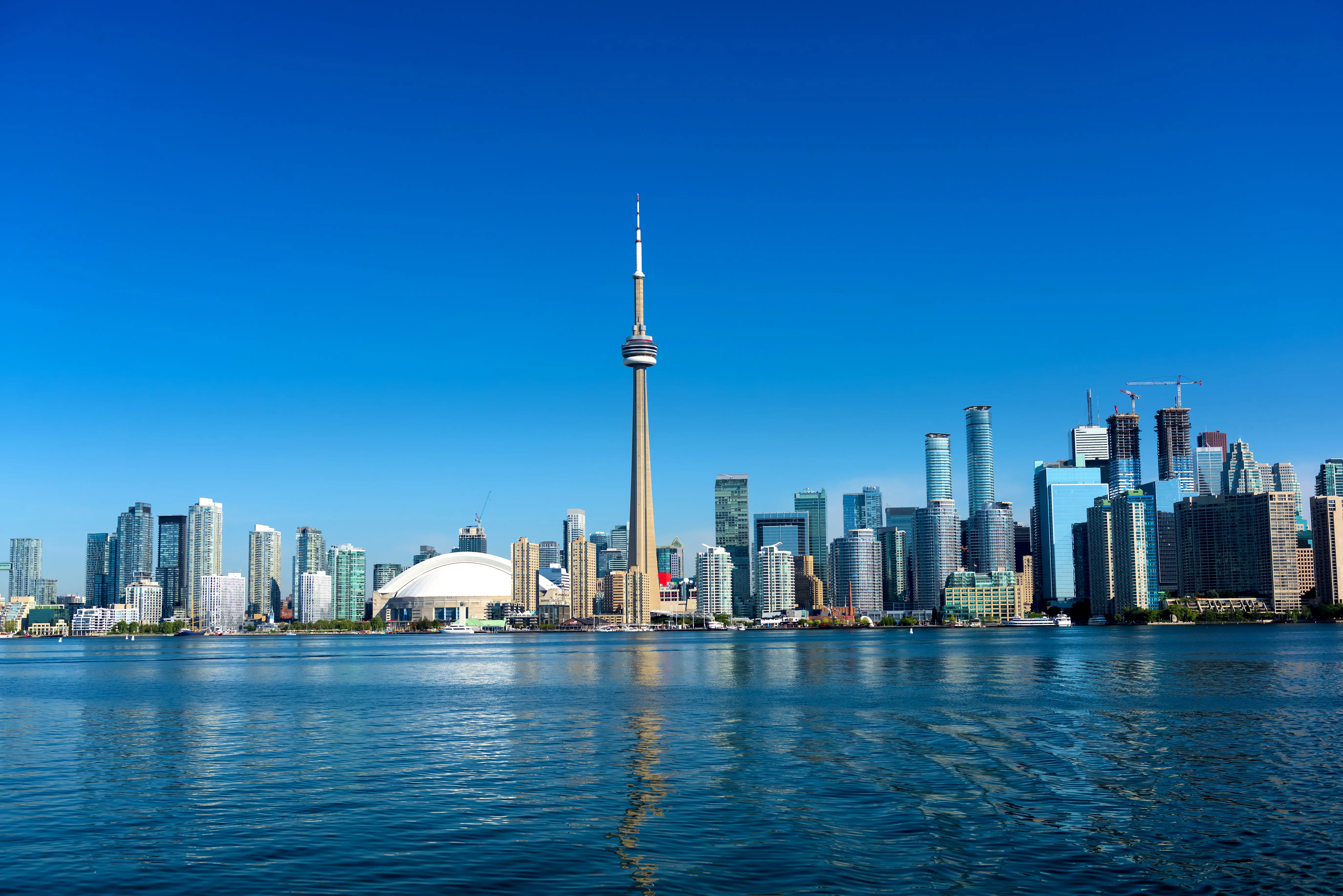 Resa till Toronto - Panoramavy över Toronto skyline med CN Tower och reflektioner i vattnet under klarblå himmel.