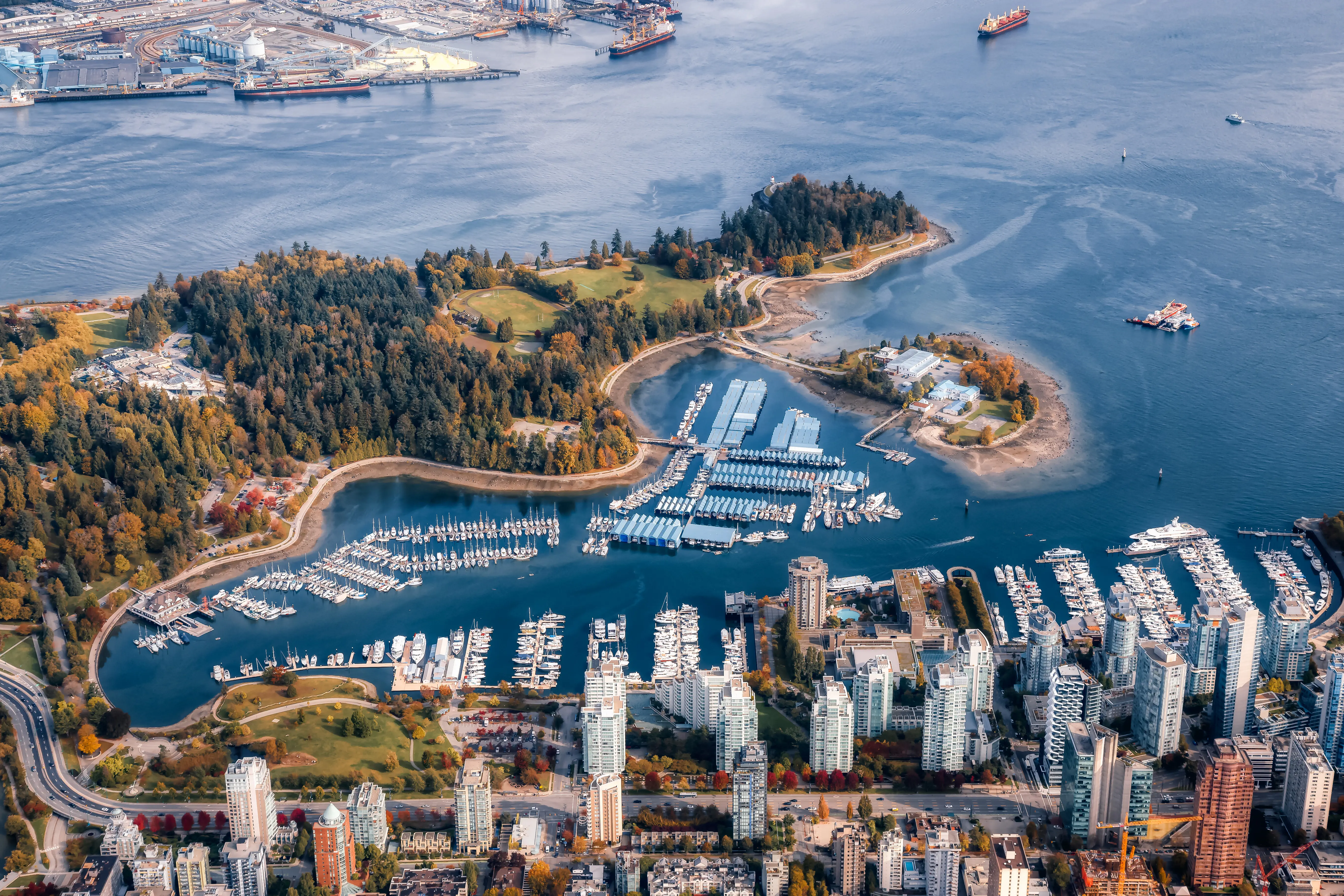 Resa till Vancouver - Flygfoto över hamn och stad med båtkajer och höghus i förgrunden, grönskande parkområde och industrihamn i bakgrunden.