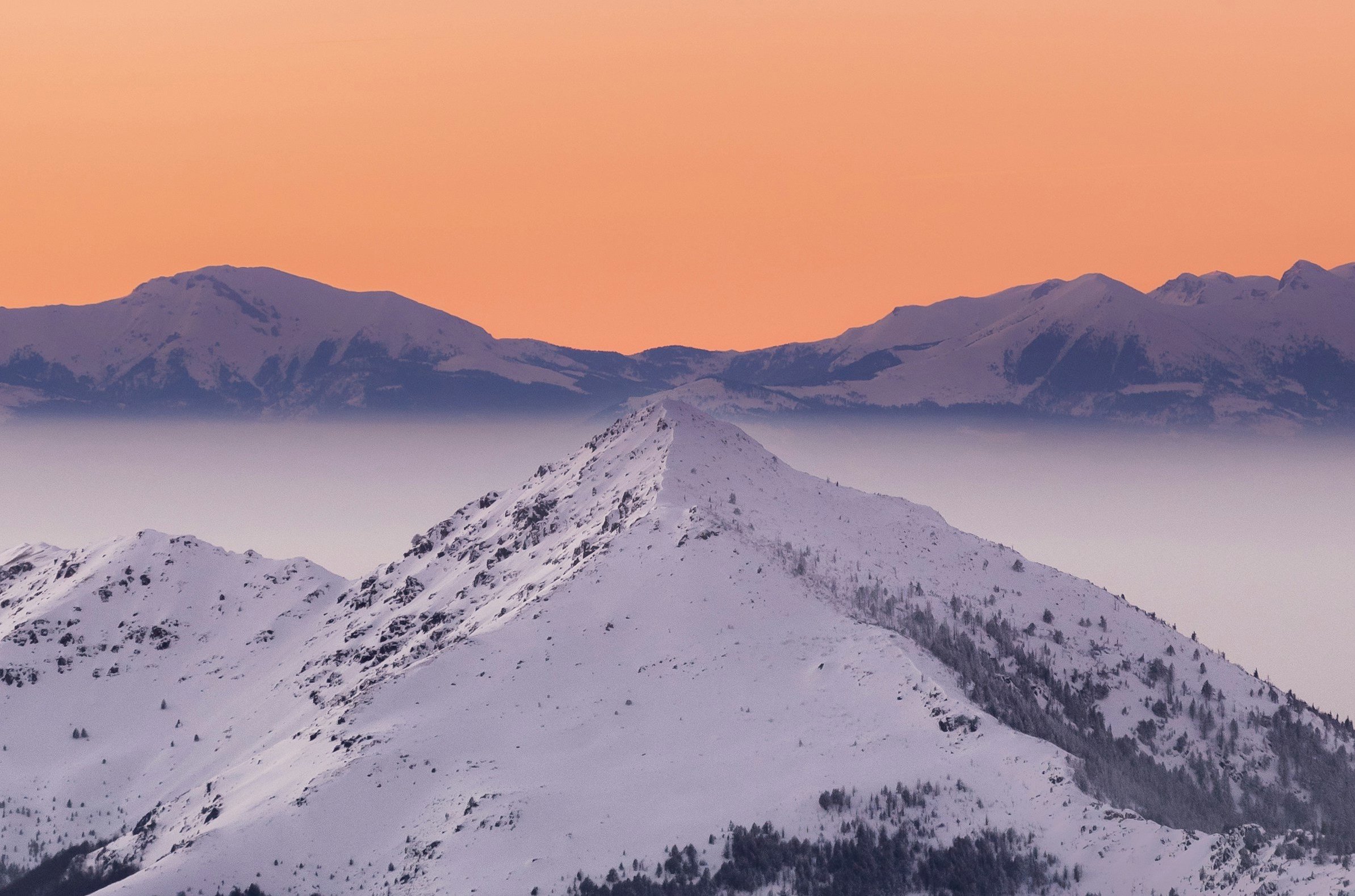 Solnedgång över ett berg och snötäckta backar i Brezovica med en orange himmel i bakgrunden