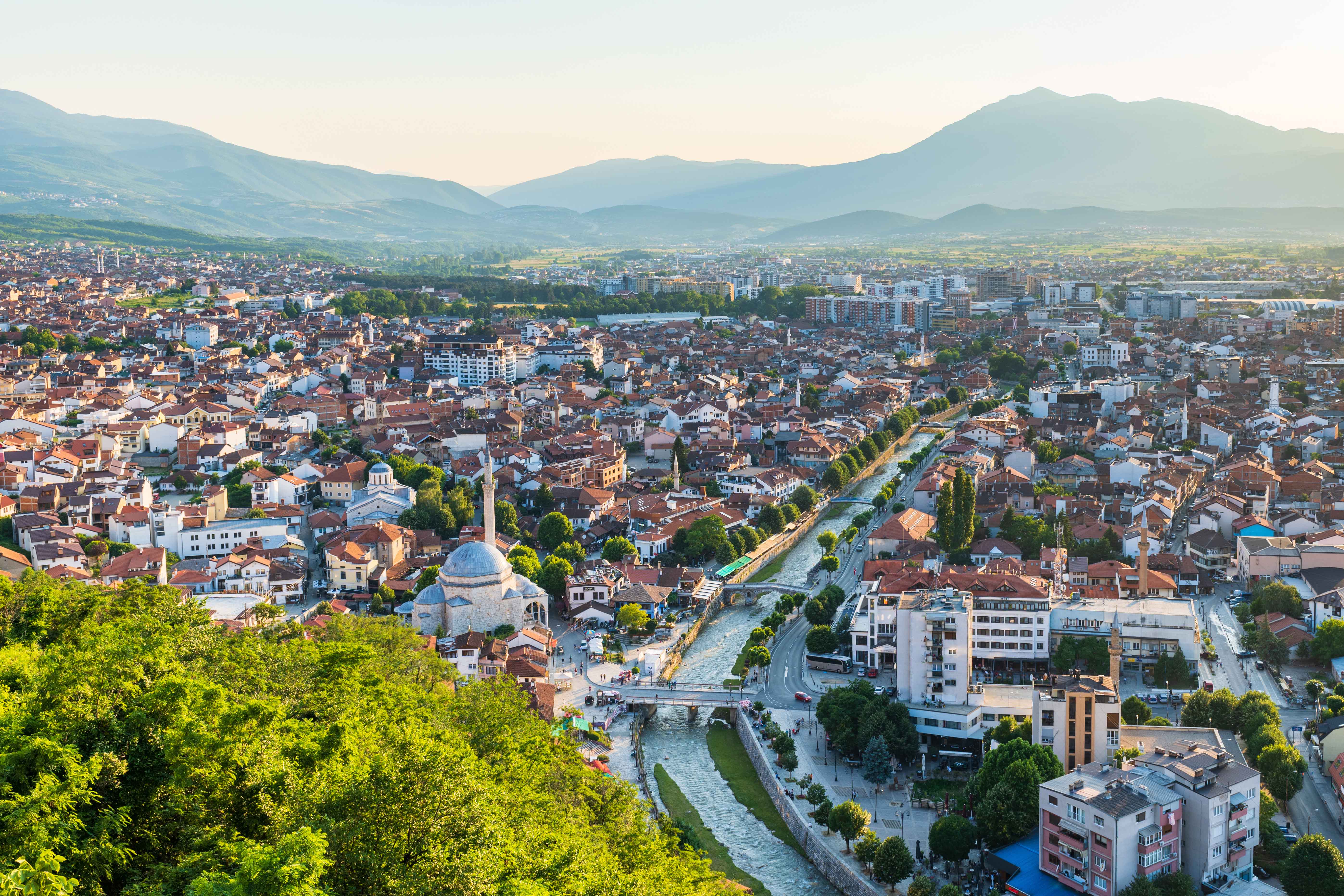 Resa till Kosovo - Panorama bild över grönskande stad med berg i bakgrunden i Kosovo