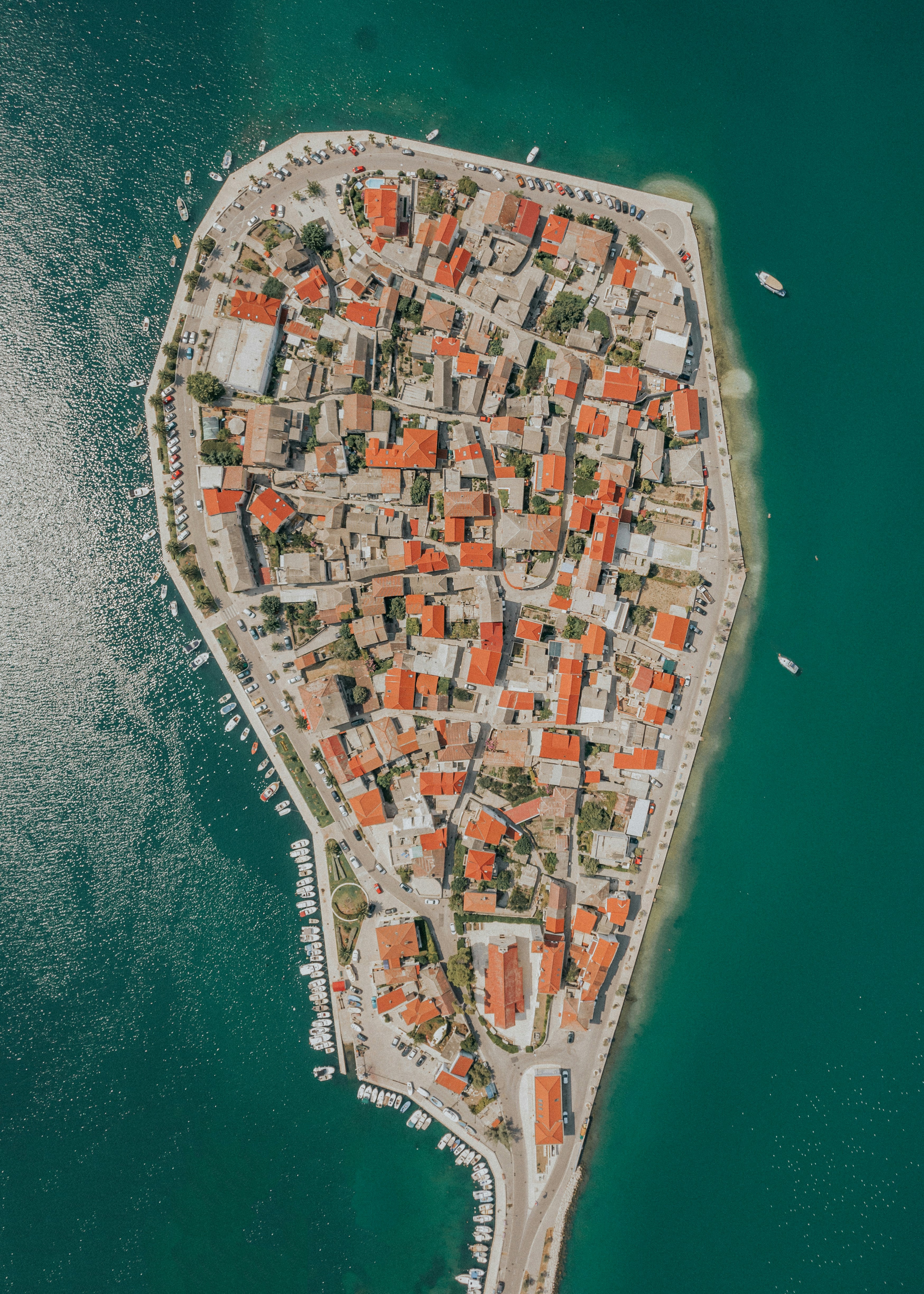 Flygbild över en pittoresk halvö med röda tak och båtar längs kusten i kristallklart vatten i Kroatien.