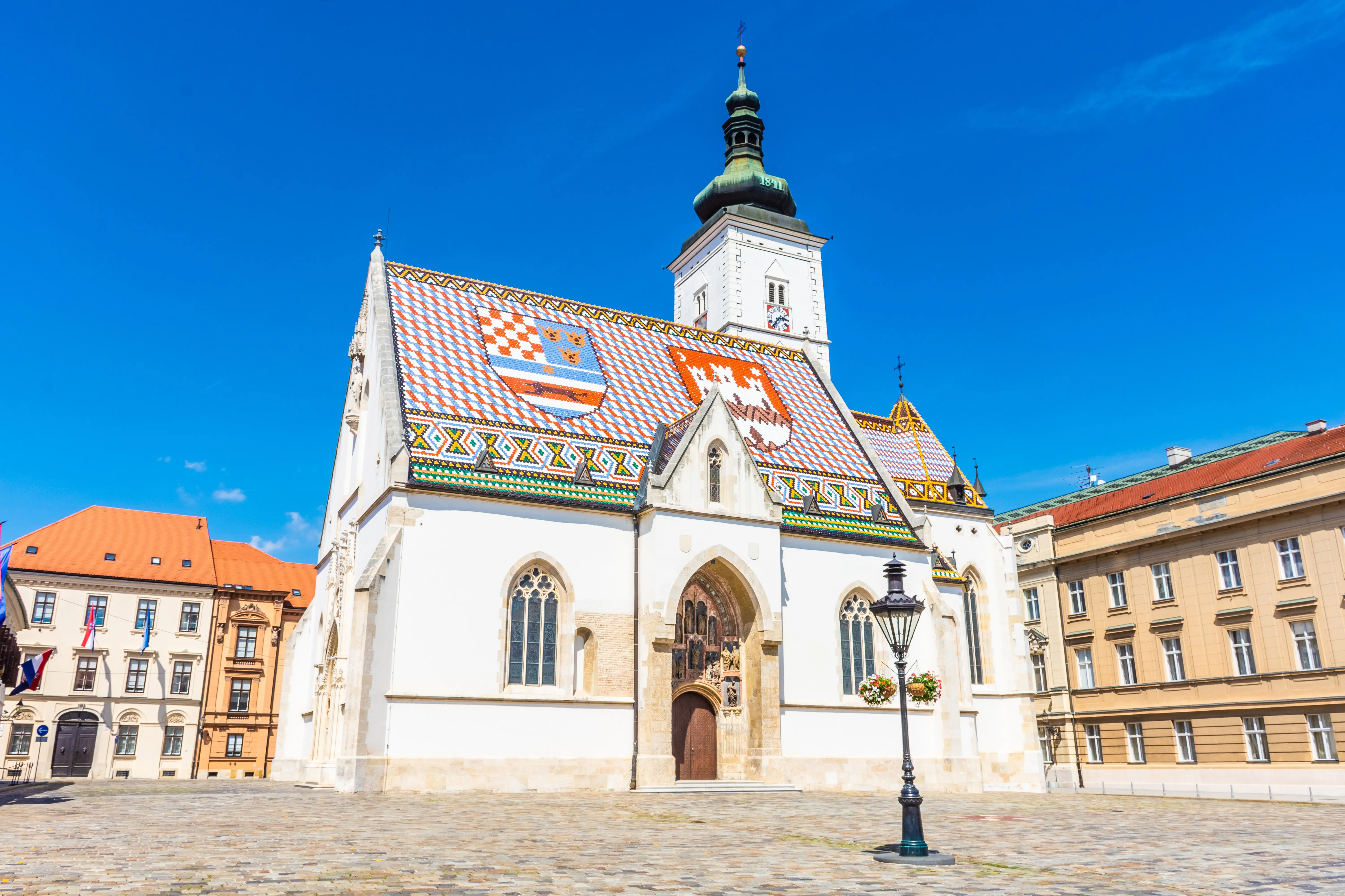 Resa till Zagreb - Kyrka med färgglatt tak och klocktorn under blå himmel, europeisk arkitektur.