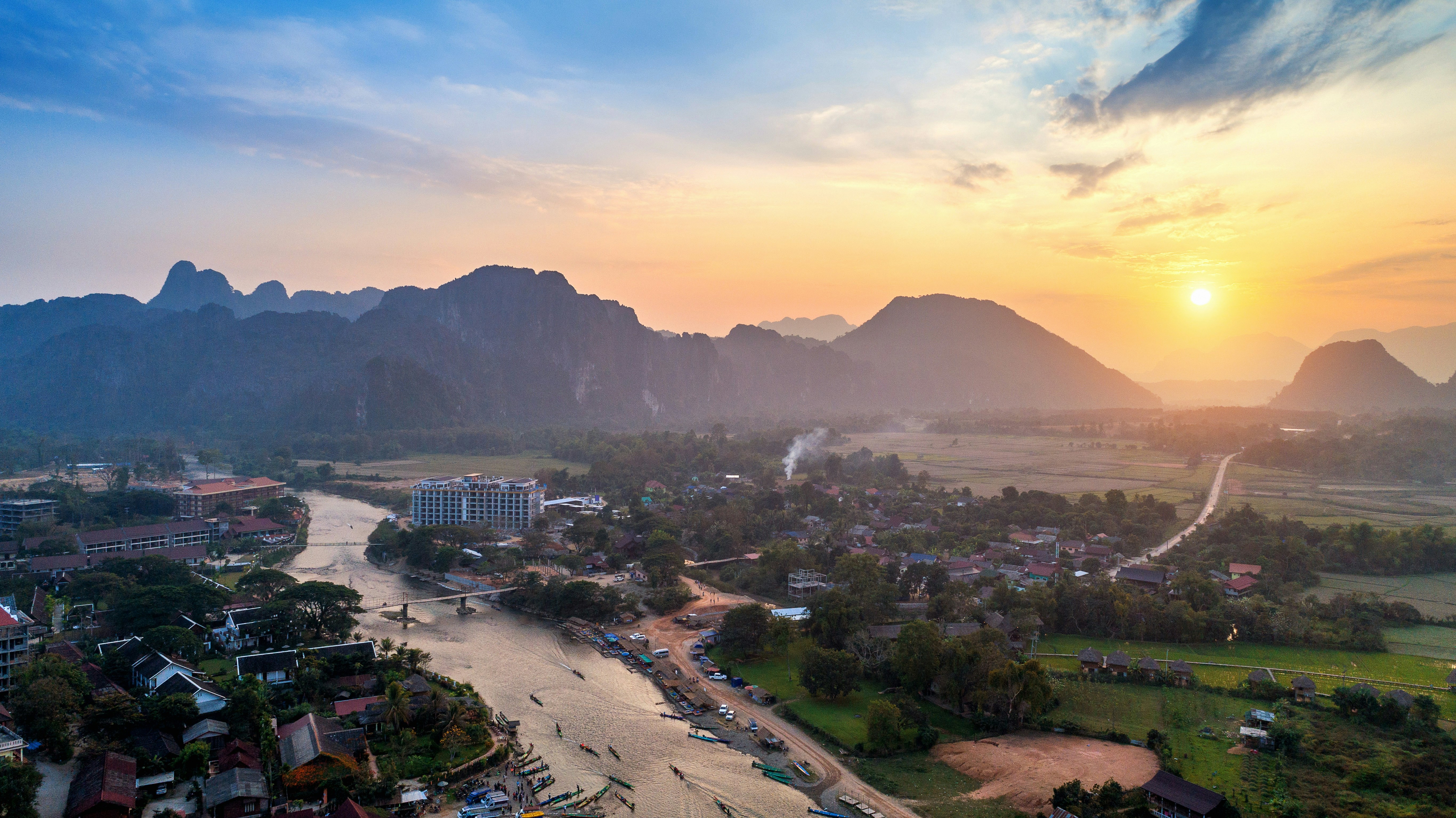 Panoramisk vy över en flod genom en djungel med berg och solnedgång i bakgrunden i Laos