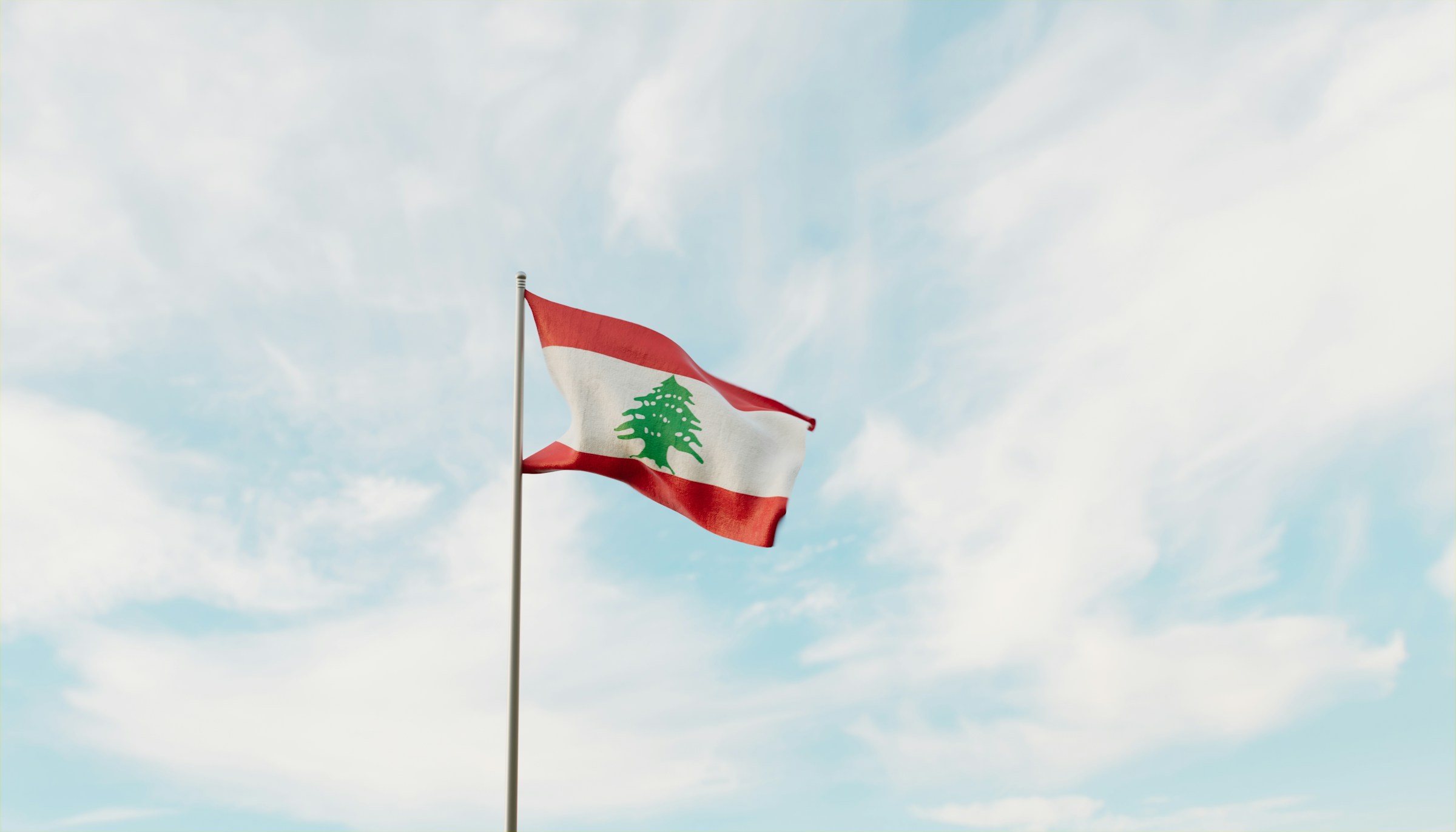 Libanons flagga vajar mot en klarblå himmel med lätta moln.