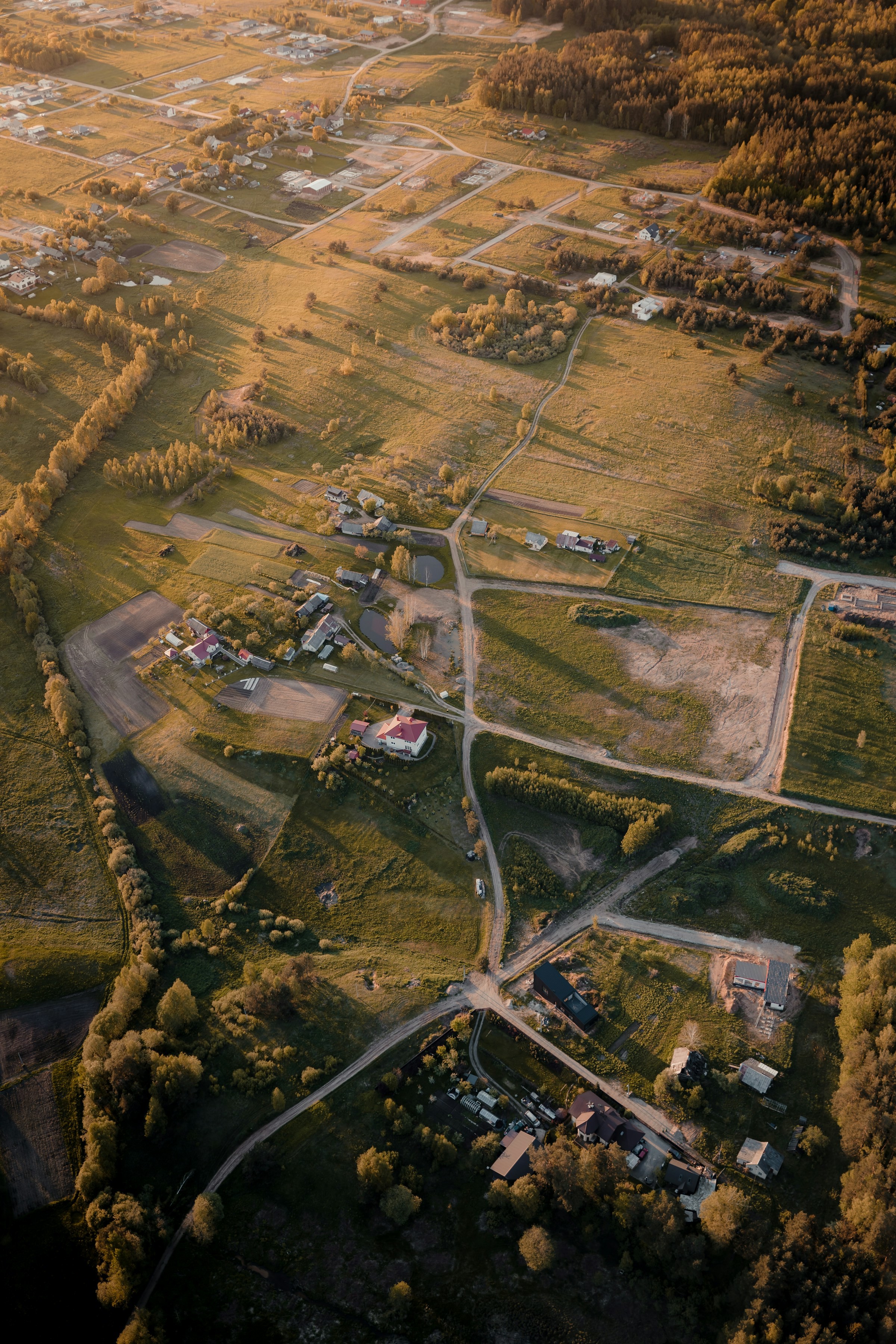 Flygfoto av en idyllisk landsbygd vid solnedgång med vägar och hus i Litauen.